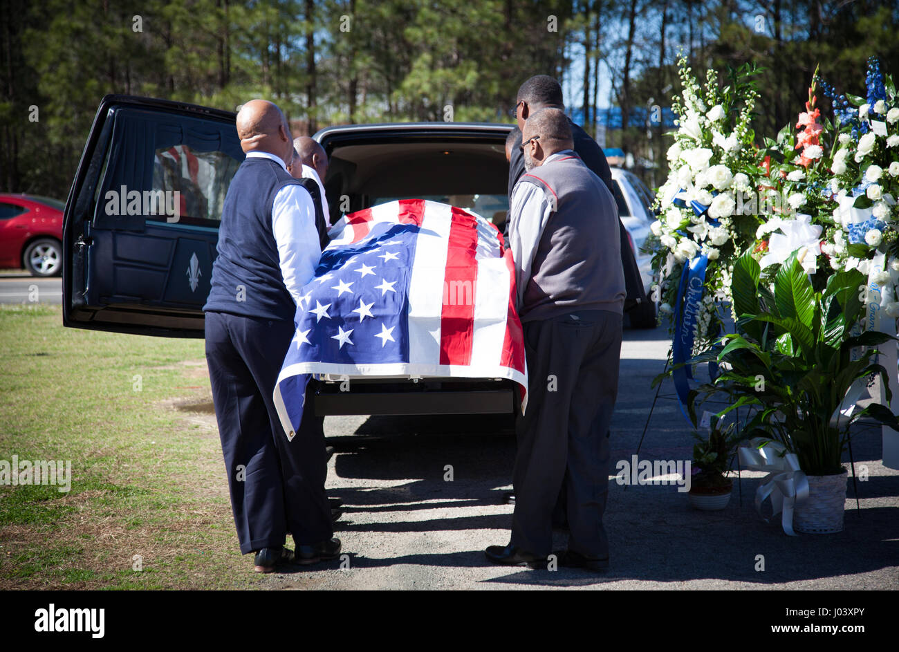 Sargträger laden einen Fahne drapiert Sarg in der Rückseite des einen Leichenwagen nach einer Beerdigung. Stockfoto