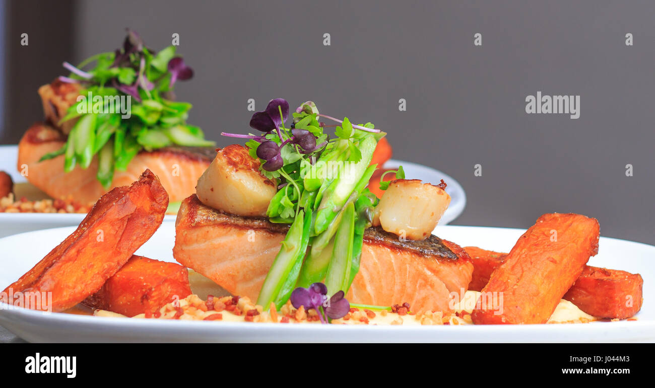 Knusprige Haut Pfanne gebratenes Lachsfilet mit Blumenkohl-Püree, Süßkartoffel, Jakobsmuscheln, Spargel, Speck bröckeln, Chiliöl Stockfoto