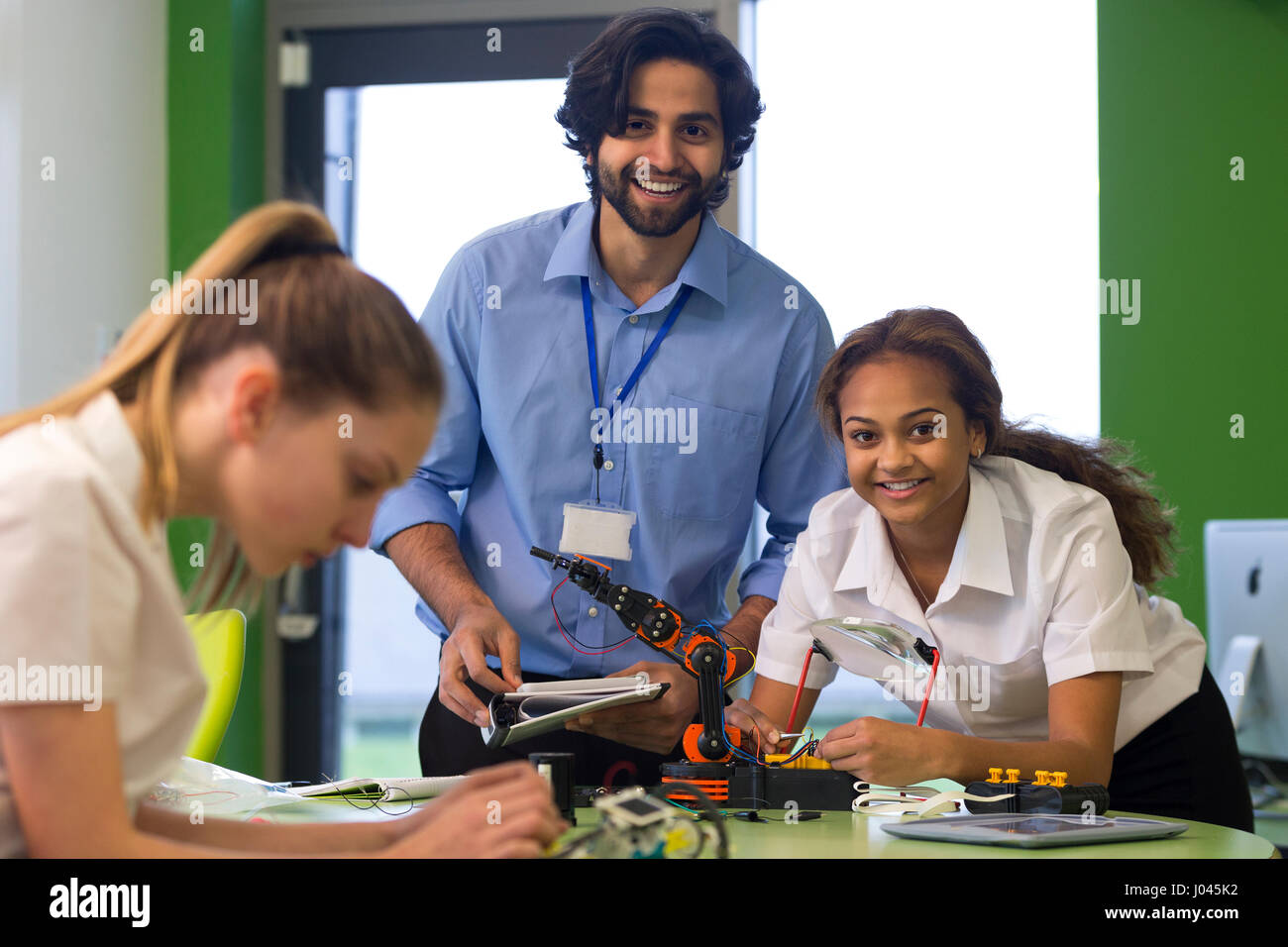 Lehrer und Schüler Lächeln für die Kamera während des Baus eines Roboterarms. Ein anderer Student ist außerhalb des Fokus im Vordergrund. Stockfoto