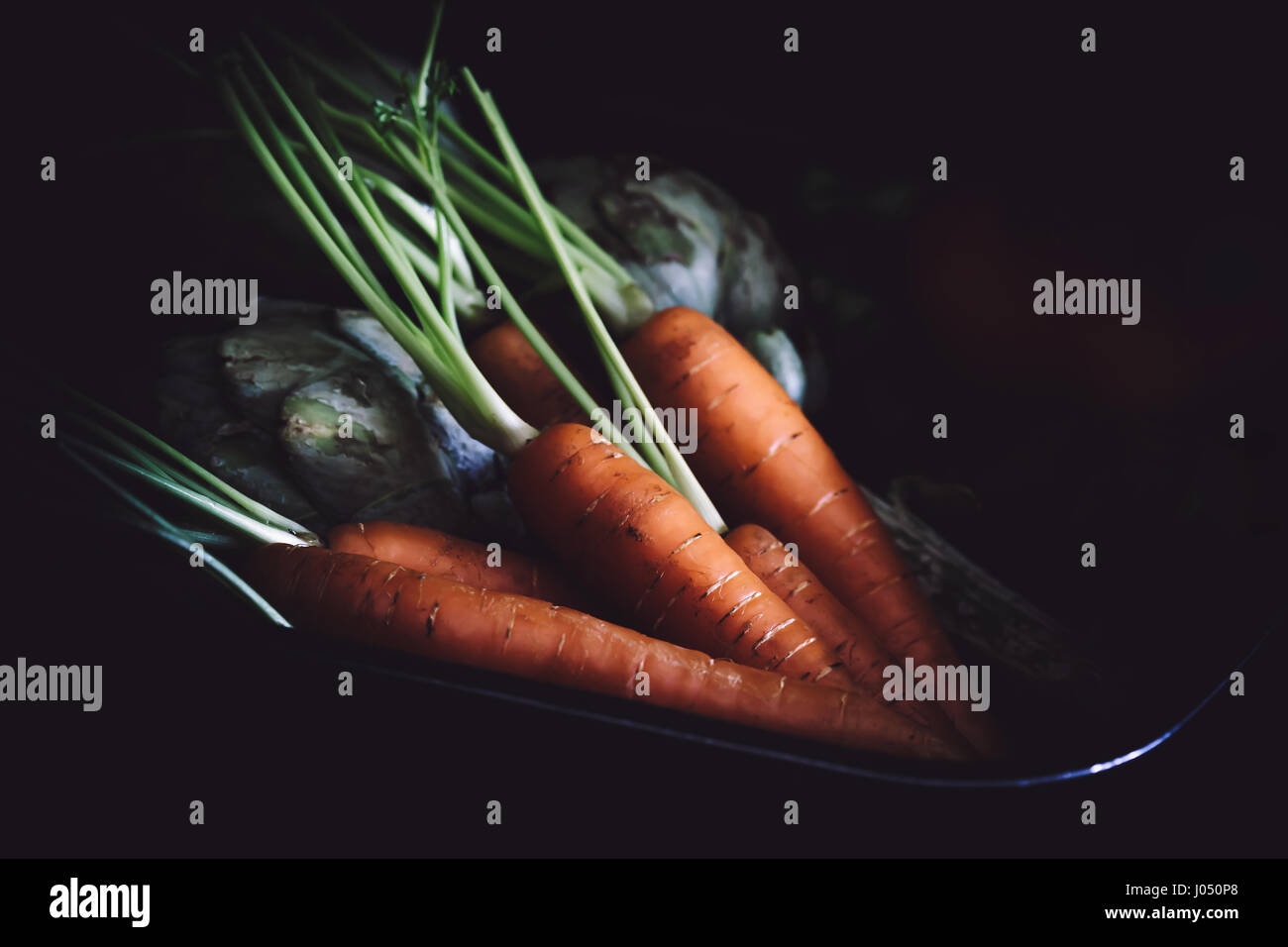 Topf mit Karotten und Artischocken auf schwarzem Hintergrund. Stockfoto