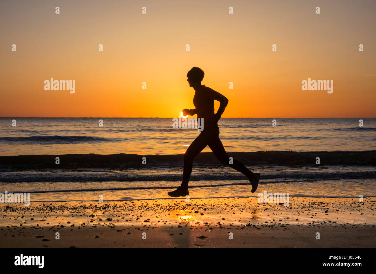 Jogger, Läufer, Mann, der bei Sonnenaufgang am Strand läuft. GROSSBRITANNIEN Stockfoto