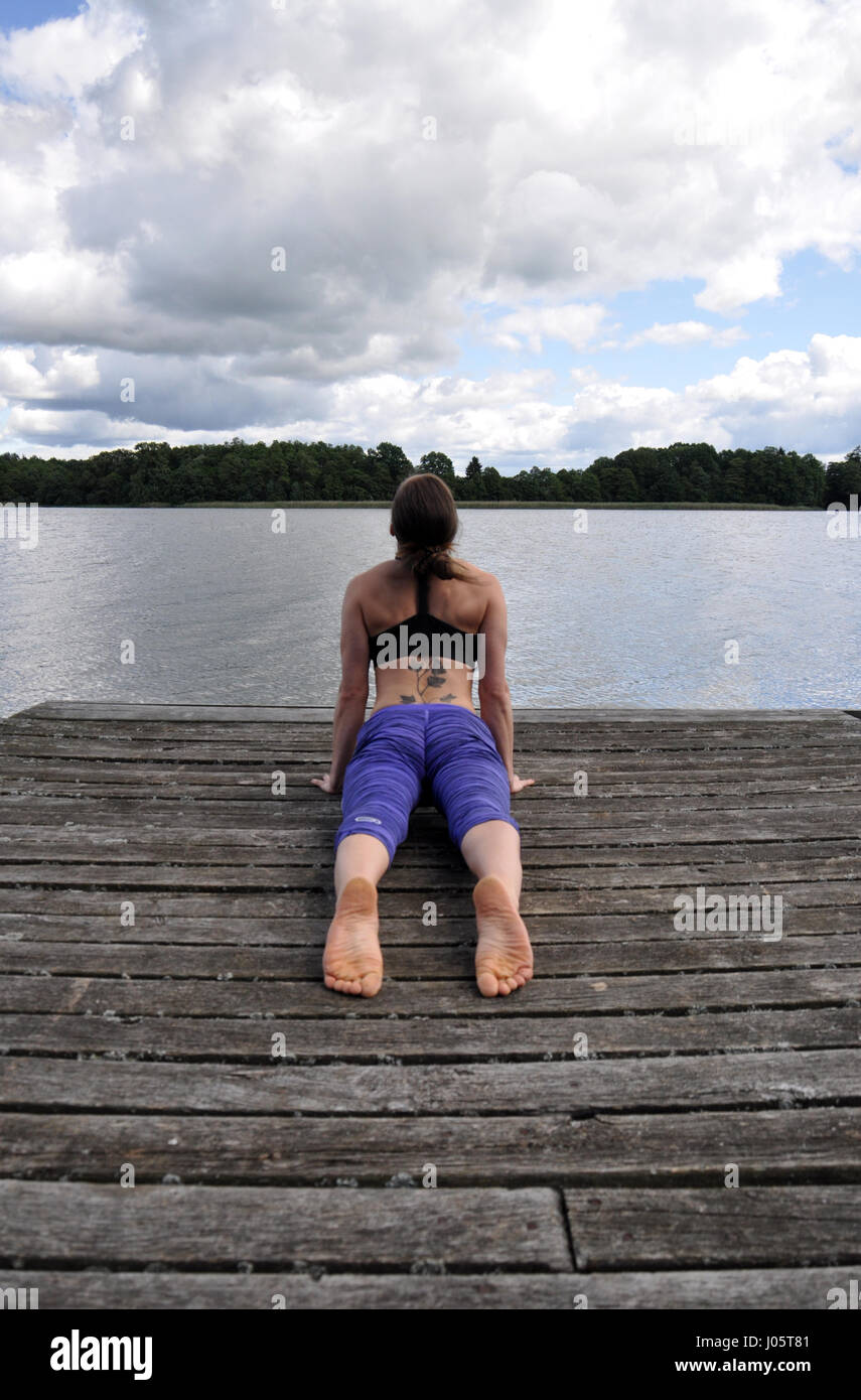 Junge aktive Frau tun Yoga-Positionen auf den Holzsteg am See im polnischen Countsydie in Masuren region Stockfoto