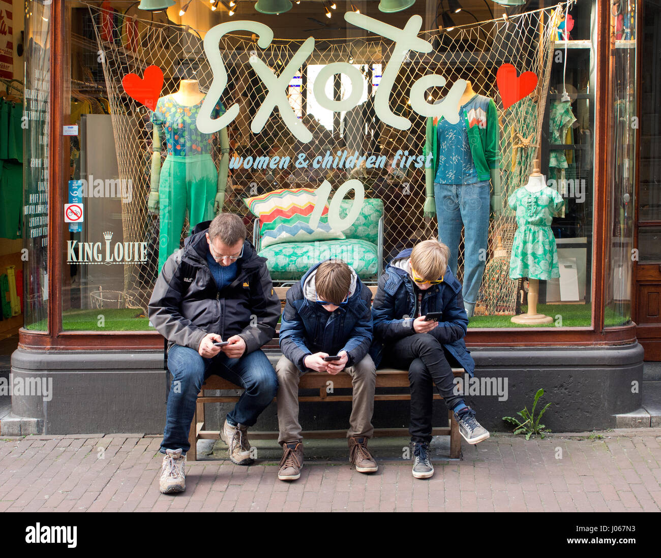 Vater und Söhne spielen mit Smartphones in einer Straße in Amsterdam Stockfoto