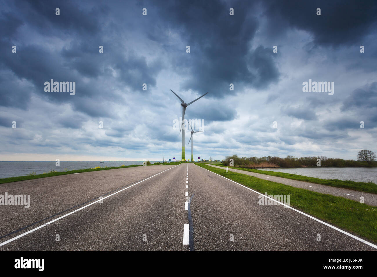 Schöne asphaltierte Straße mit Windkraftanlagen zur Stromerzeugung. Windmühlen zur Stromerzeugung. Landschaft mit Strasse, grünen Rasen und wind m Stockfoto