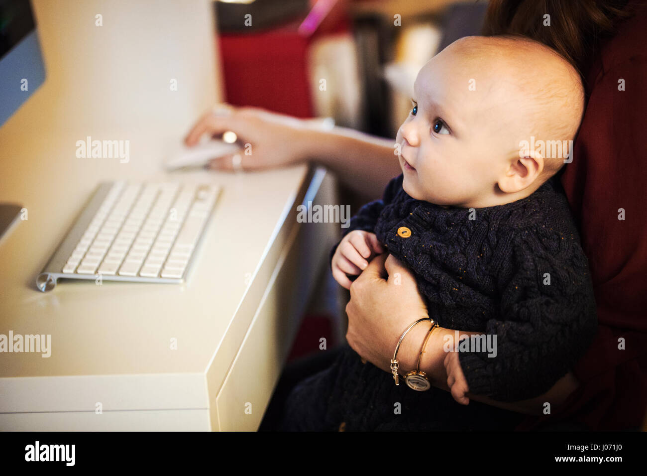 Ein Baby sitzt auf einem Erwachsenen Knie, einem Computer-Bildschirm betrachten, Stockfoto