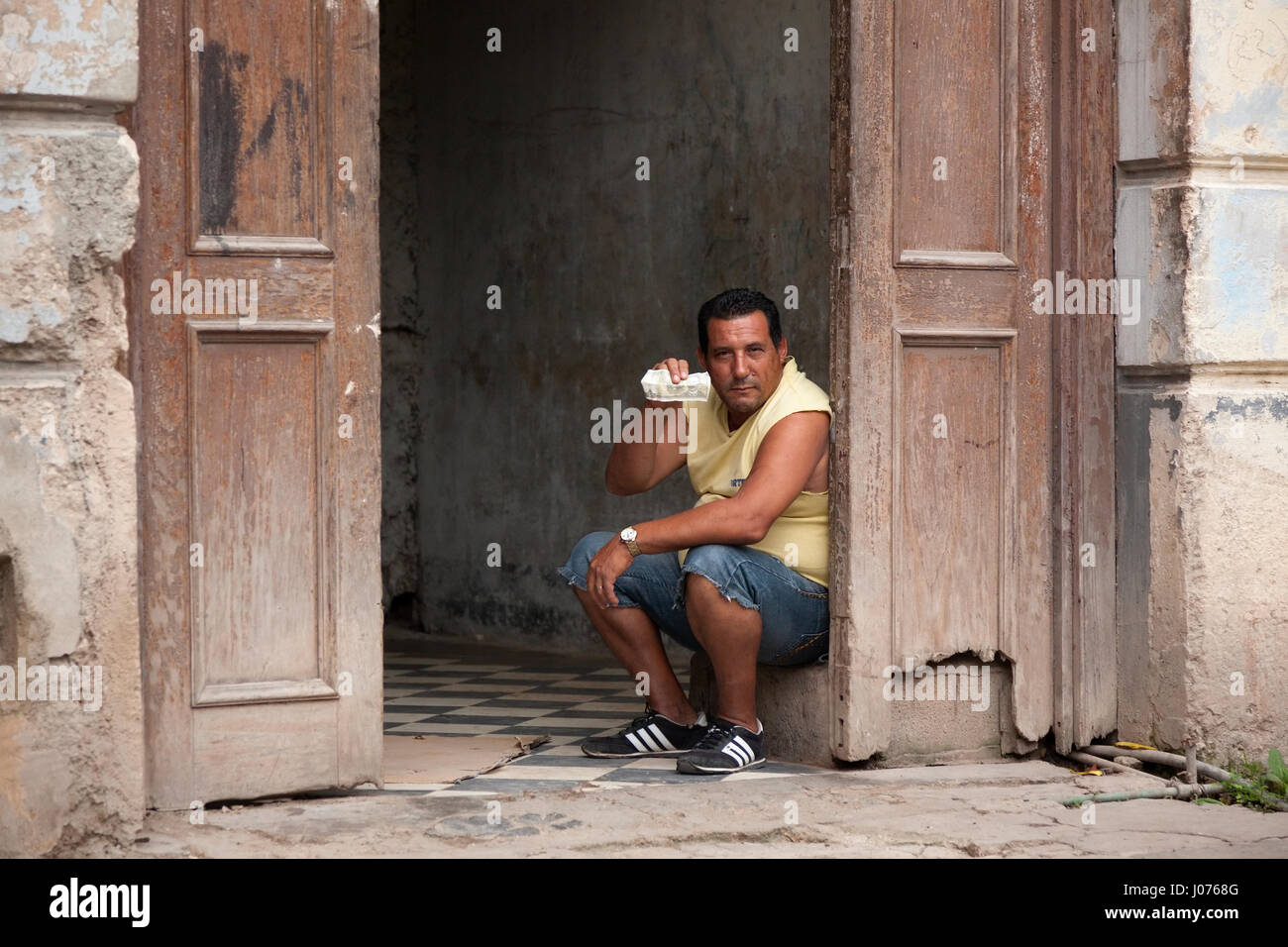 Ein Mann hält ein kubanischer Peso sitzen im Inneren eines Gebäudes in Alt-Havanna, Kuba. Stockfoto