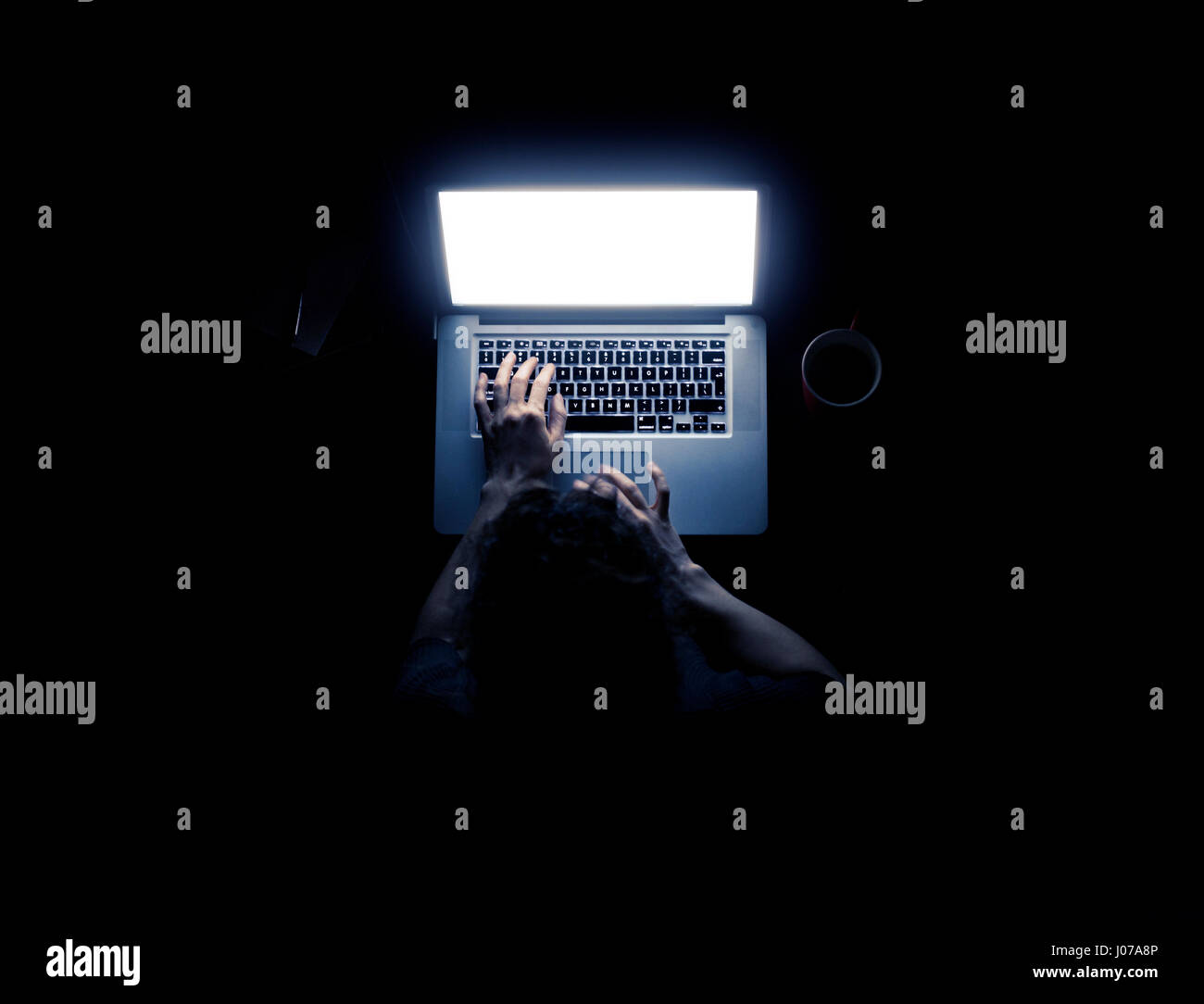 Frau mit einem Laptop-Computer in der Dunkelheit mit ihren Händen, die von dem Computer-Bildschirm auf schwarzem Hintergrund isoliert erhellt Stockfoto