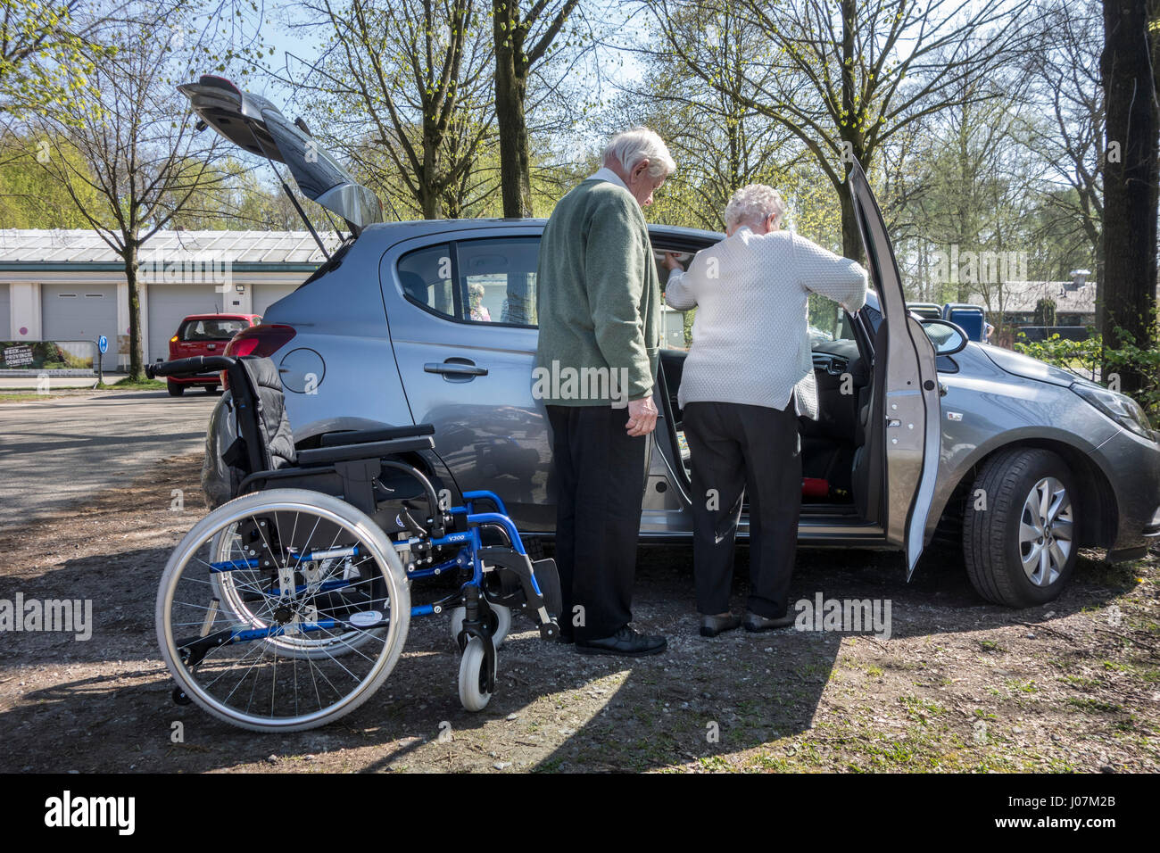 Pensionierter Mann helfen körperlich deaktiviert ältere Frau aus Rollstuhl Eingabe Auto am Parkplatz Stockfoto