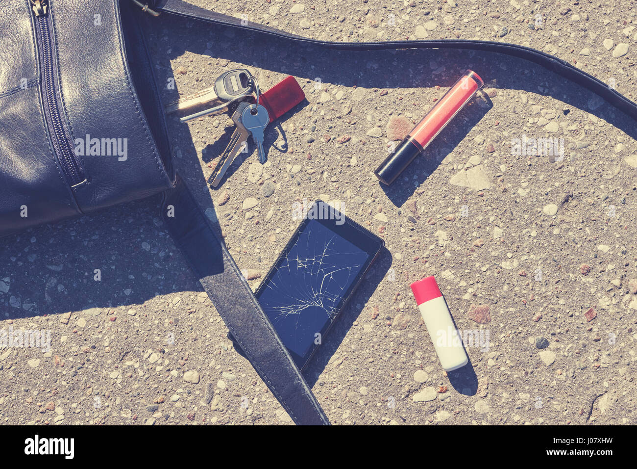 Nahaufnahme einer Handtasche, Handy mit zerbrochenen Bildschirm, Schlüsseln und Lippenstift auf Asphalt Straße, Darstellung, Farbe toning angewandte. Stockfoto