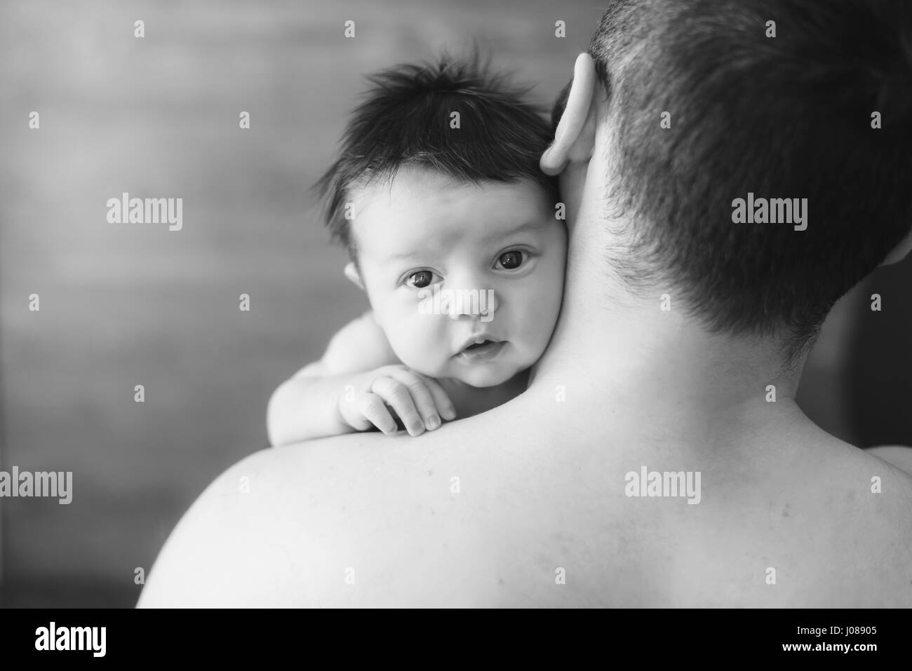 Neugeborenes Baby und Papa. Vater mit Baby über die Schulter schauen. Das Kind schaut die Kamera. schwarz / weiß Foto. Stockfoto