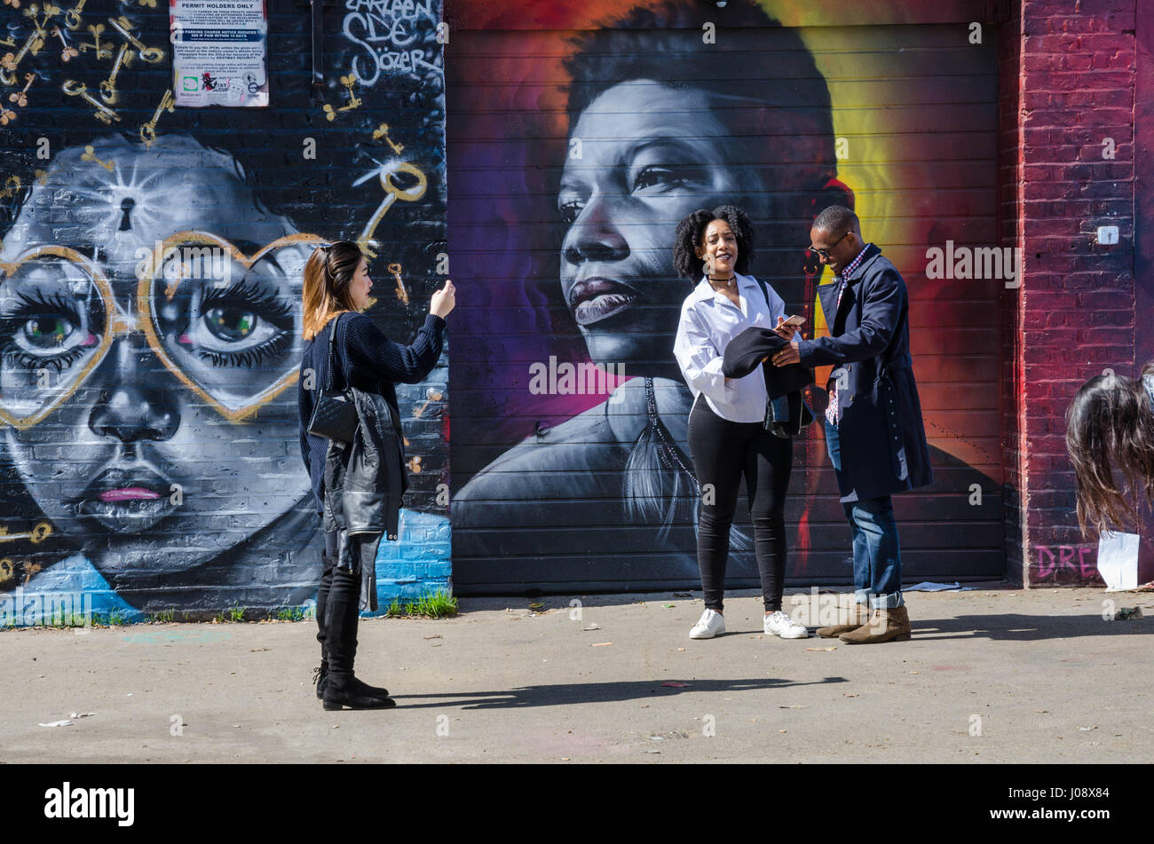 Touristen bewundern und Pose für Fotos mit den lebendigen, farbenfrohen Street sind die Wände von einem Parkplatz aus Brick Lane in London abdeckt. Stockfoto