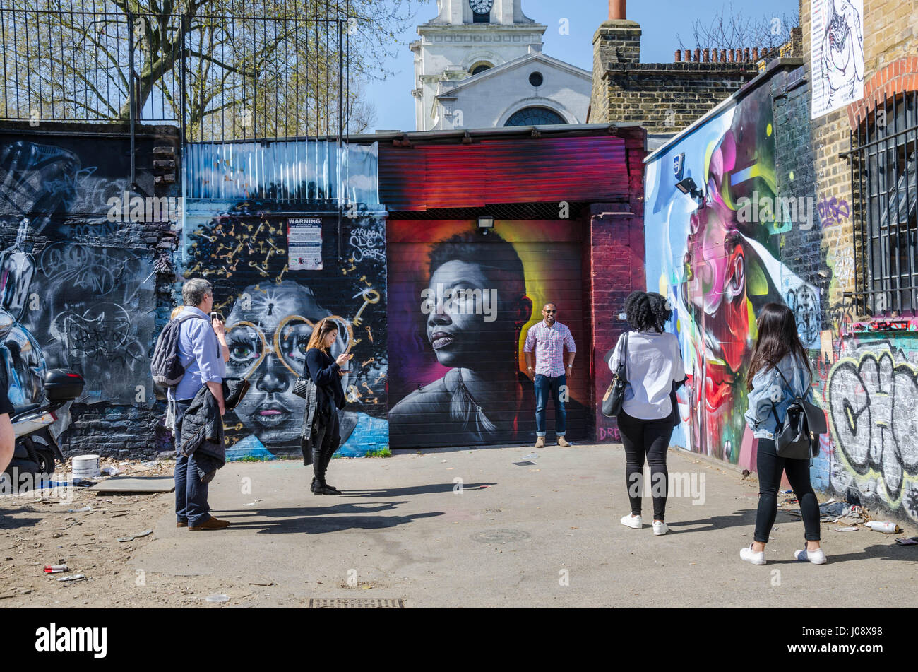 Touristen bewundern und Pose für Fotos mit den lebendigen, farbenfrohen Street sind die Wände von einem Parkplatz aus Brick Lane in London abdeckt. Stockfoto