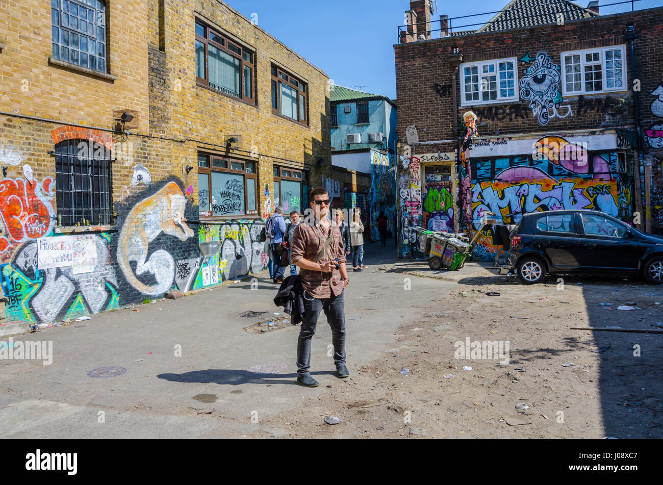 Ein Tourist steht und bewundert die Straße Kunstwerken an den Wänden einen Parkplatz direkt an der Brick Lane im Osten Londons. Stockfoto