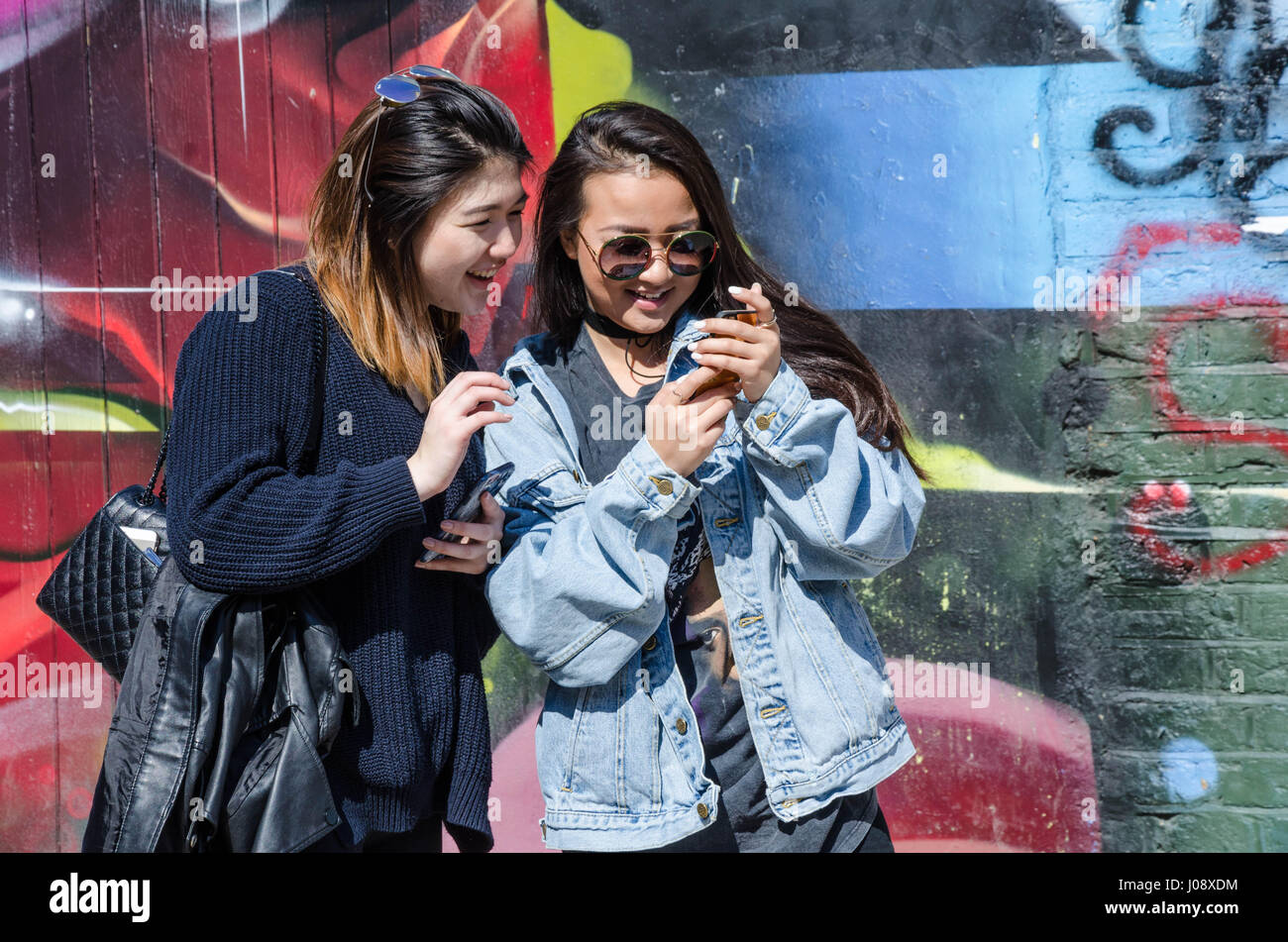 Ein paar Touristen Freunde stehen und bewundern Sie ein Selbstporträt, das sie gerade auf einem Smartphone vor der street Art an Wänden in der Nähe von Brick Lane genommen haben. Stockfoto