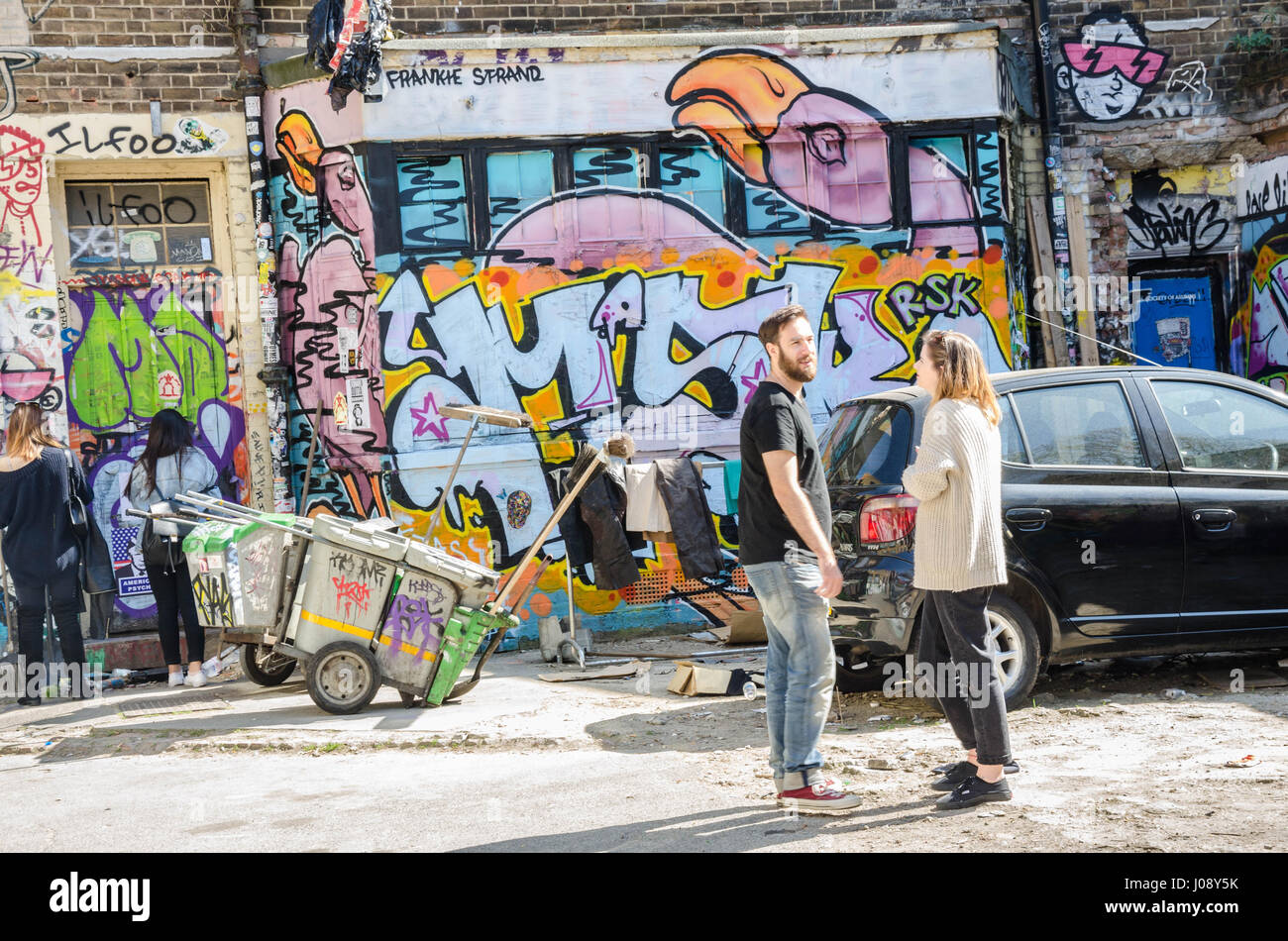 Touristen bewundern die bunten Wandmalereien an den Wänden ein Parkplatz direkt an der Brick Lane im Osten Londons. Stockfoto