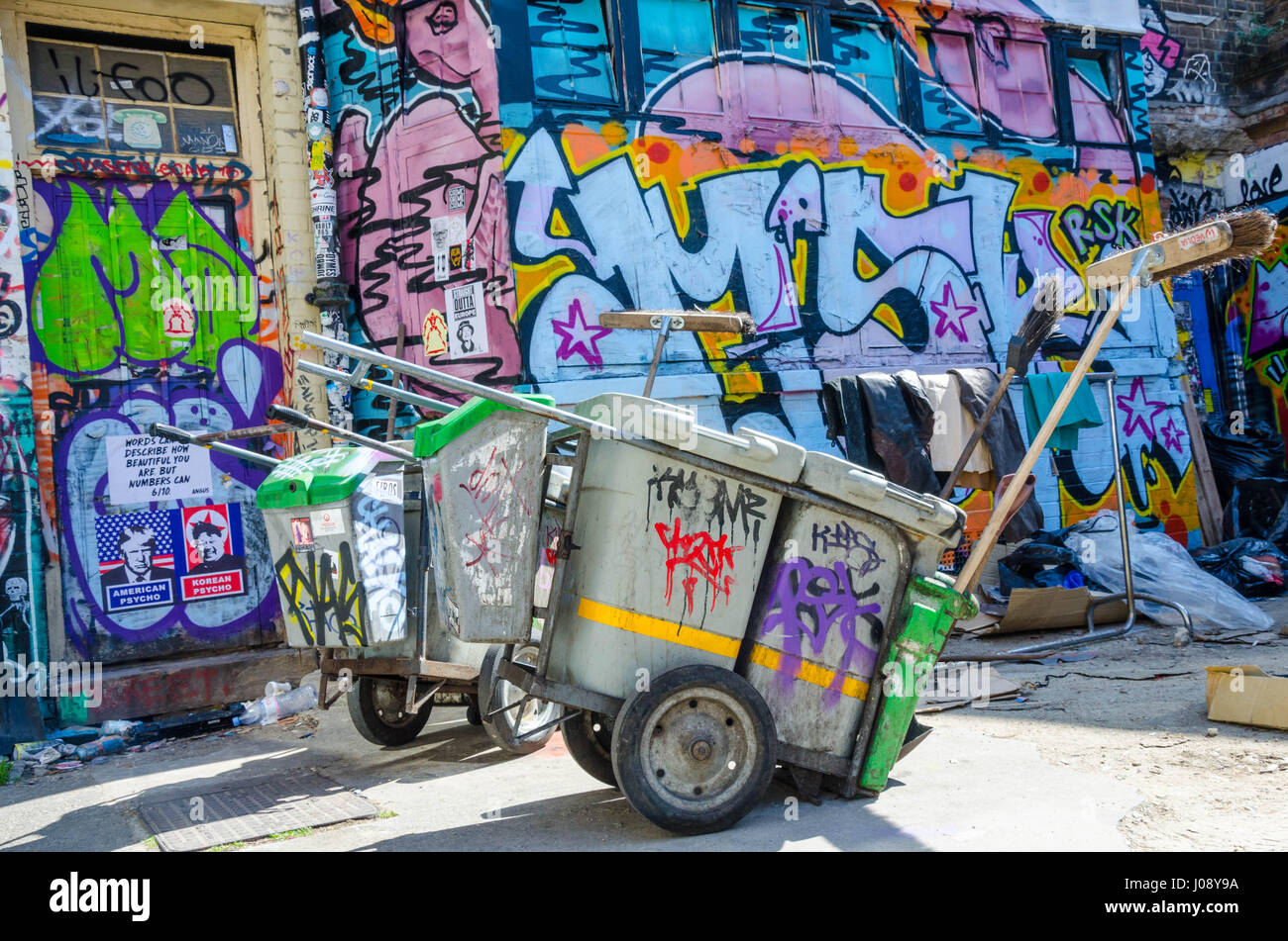 Ein paar street Cleaners Karren sitzen in Graffiti vor einer Wand in Colouful Wandbildern bedeckt bedeckt. Direkt an der Brick Lane, East London. Stockfoto