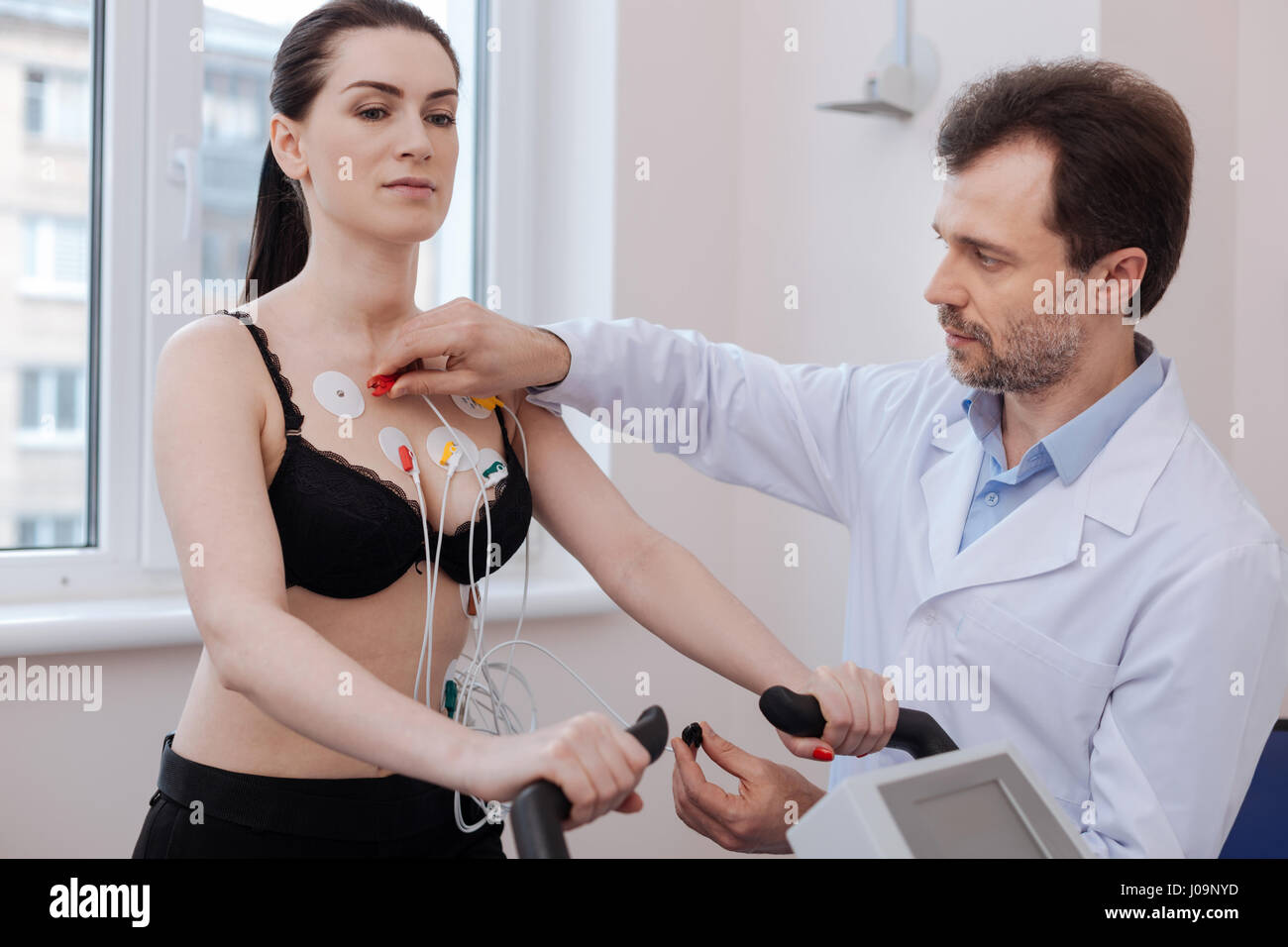 Ausgebildeter Kardiologe verbinden Elektroden konzentriert Stockfoto