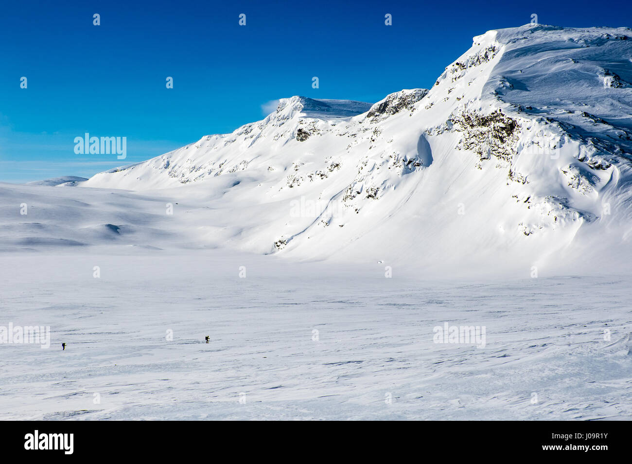 Schneebedeckte Berge, blauer Himmel, Das arktische Norwegen mit 2 Skitourengeher im Vordergrund Stockfoto
