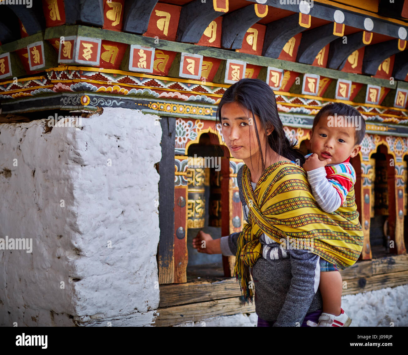 Eine Frau mit einem Baby dreht Gebetsmühlen an der Wand des Tempels Changangkha Lhakhang in Thimphu, Bhutan Stockfoto