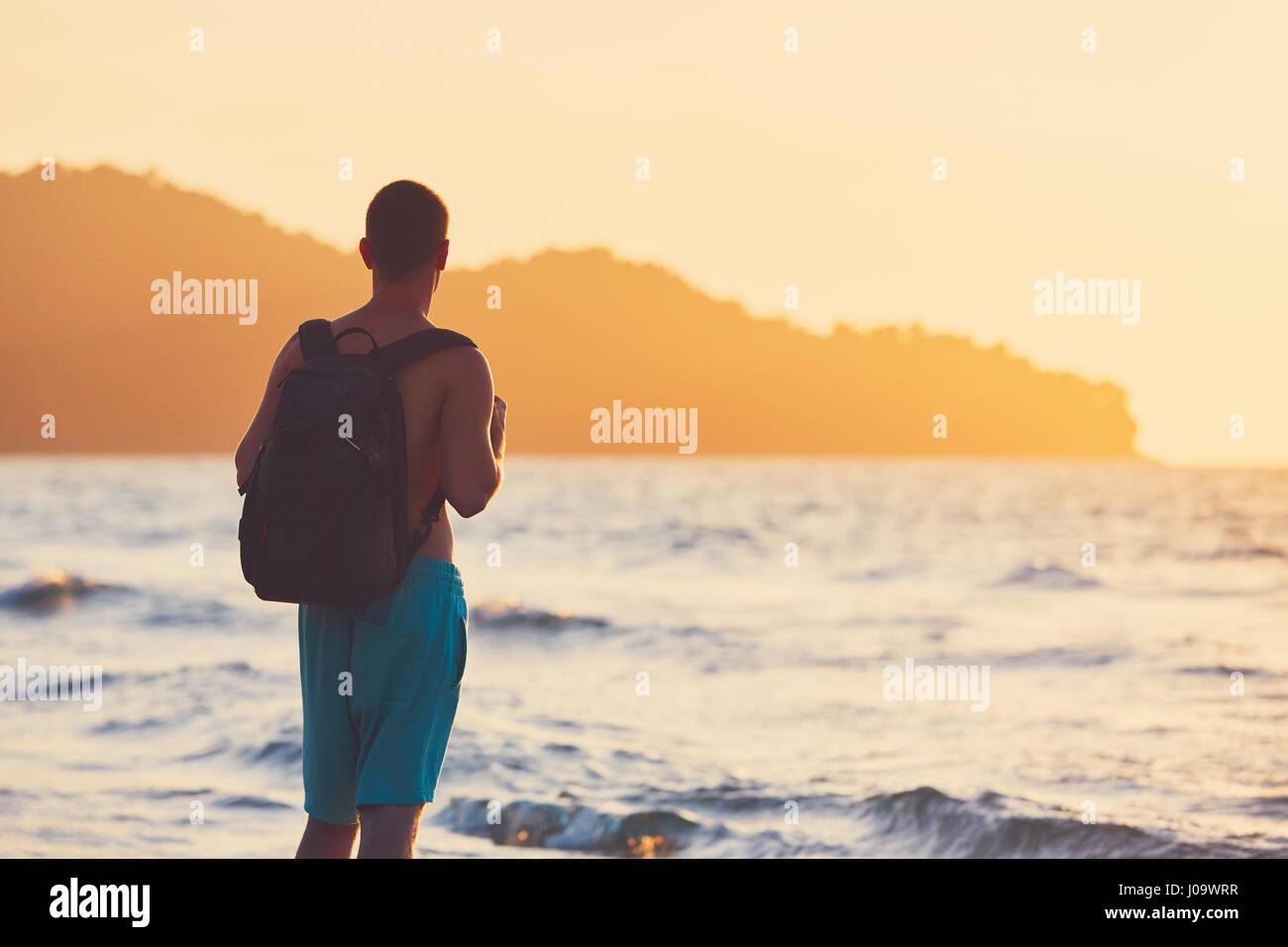 Junge Reisende mit Rucksack, die herrlichen Sonnenuntergänge beobachten. Urlaub am tropischen Strand. Stockfoto