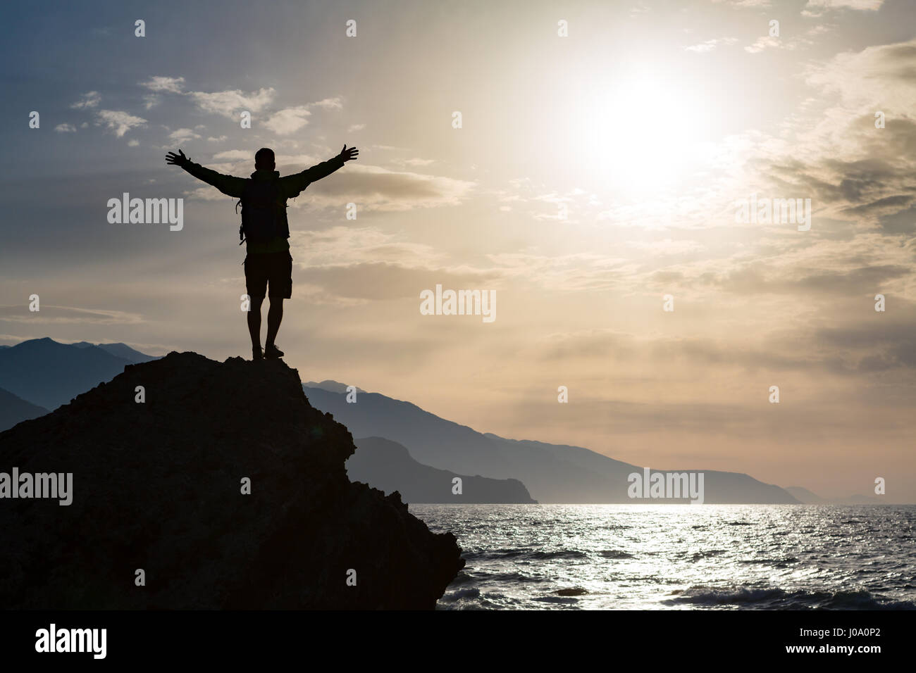 Mann mit Arme ausgestreckt feiern oder beten in schönen inspirierenden Sonnenaufgang mit Berge und Meer. Mann, Wandern oder Klettern mit Händen, genießen Sie in Stockfoto