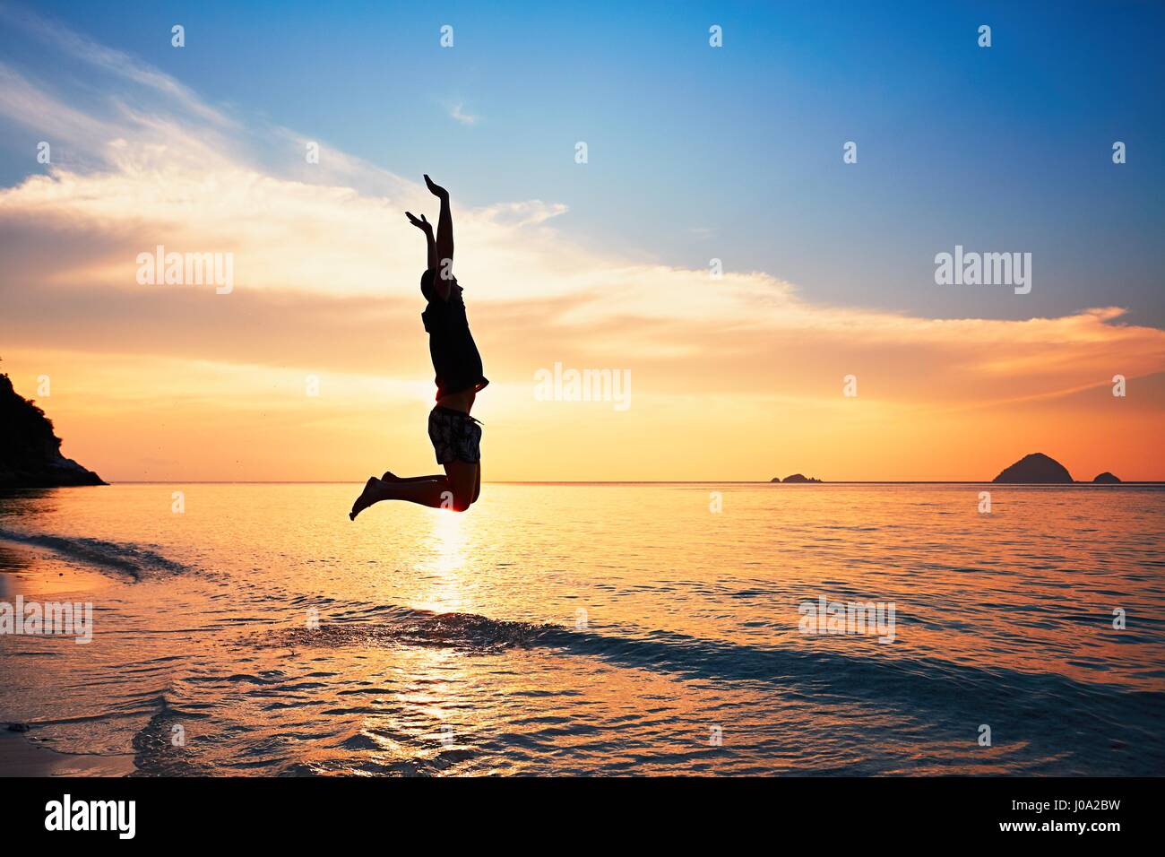 Freudiger junger Mann bei Sonnenuntergang ins Meer springen. Stockfoto