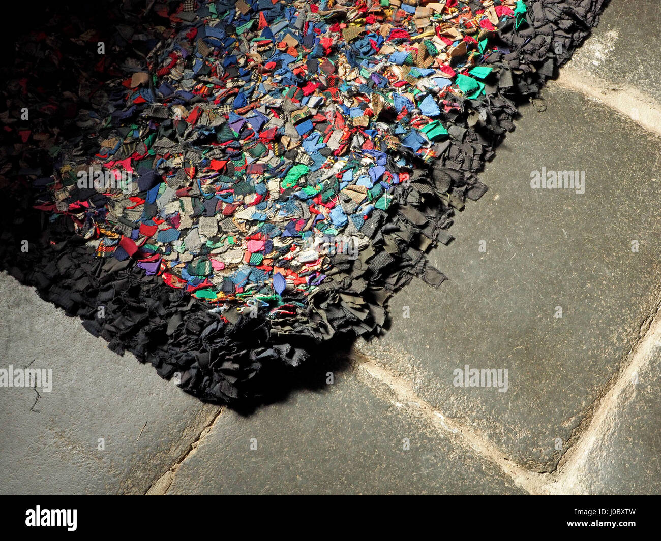 Leuchtend bunte Flickenteppich mit schwarzem Rand auf grau gekennzeichnete Schieferboden Stockfoto