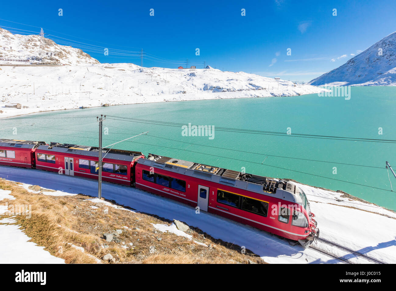 Bernina Express Zug im verschneiten Tal umgeben von See Bianco, Berninapass, Kanton Graubünden, Engadin, Schweiz Stockfoto