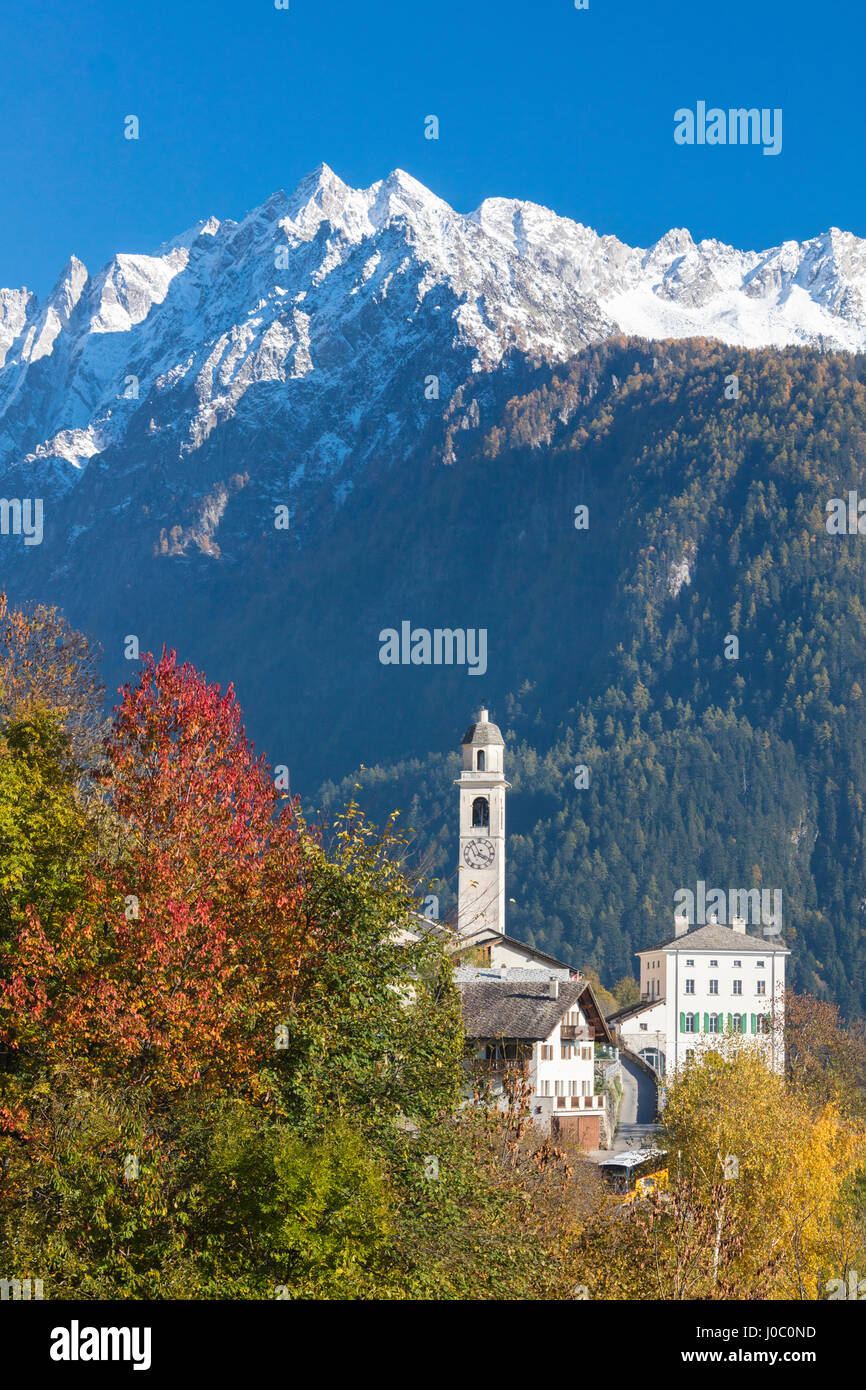Die bunten Bäume umrahmen die alpine Kirche und den schneebedeckten Gipfeln, Soglio Bergell Tal, Schweizer Alpen, Schweiz Stockfoto