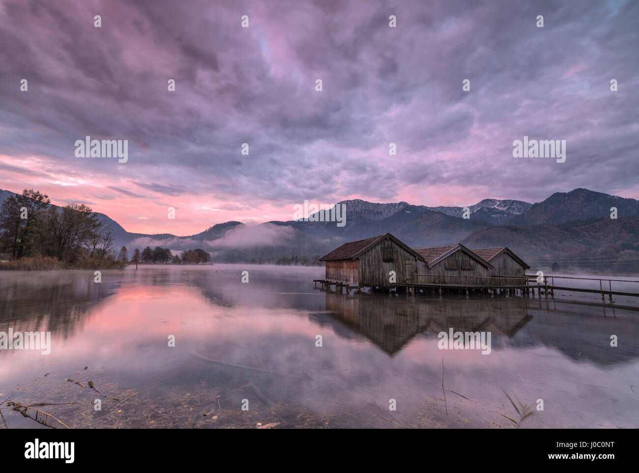 Lila Himmel bei Sonnenuntergang und hölzernen Hütten spiegeln sich im klaren Wasser des Kochelsee Schlehdorf, Bayern, Deutschland Stockfoto