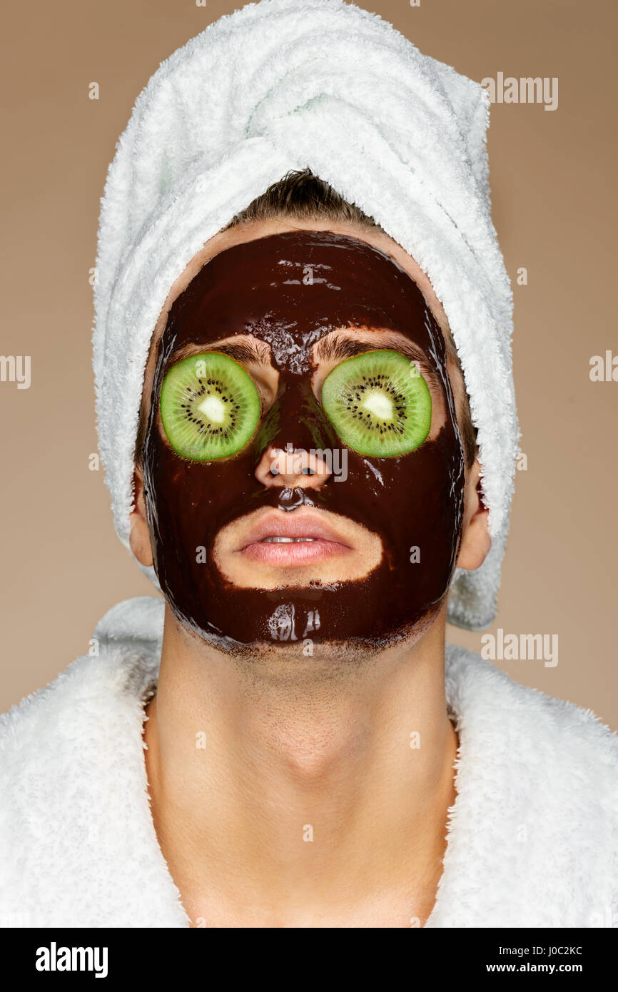 Mann mit Schokolade Mack und Kiwi Scheiben auf Augen. Porträt von gut aussehender Mann, Spa-Behandlungen erhalten. Haut-Pflege-Konzept Stockfoto