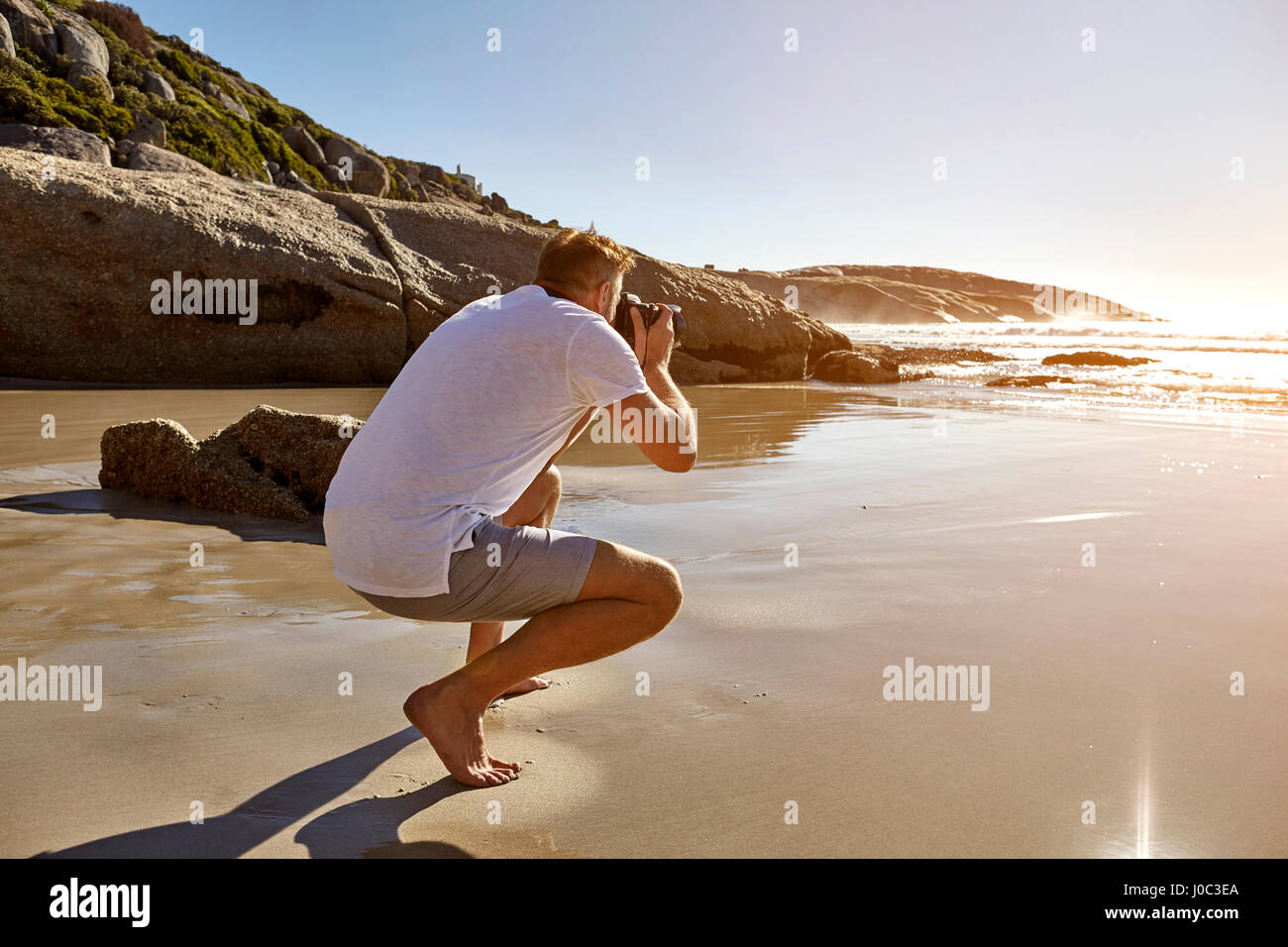 Reifer Mann kauert am Strand fotografieren View, Kapstadt, Südafrika Stockfoto
