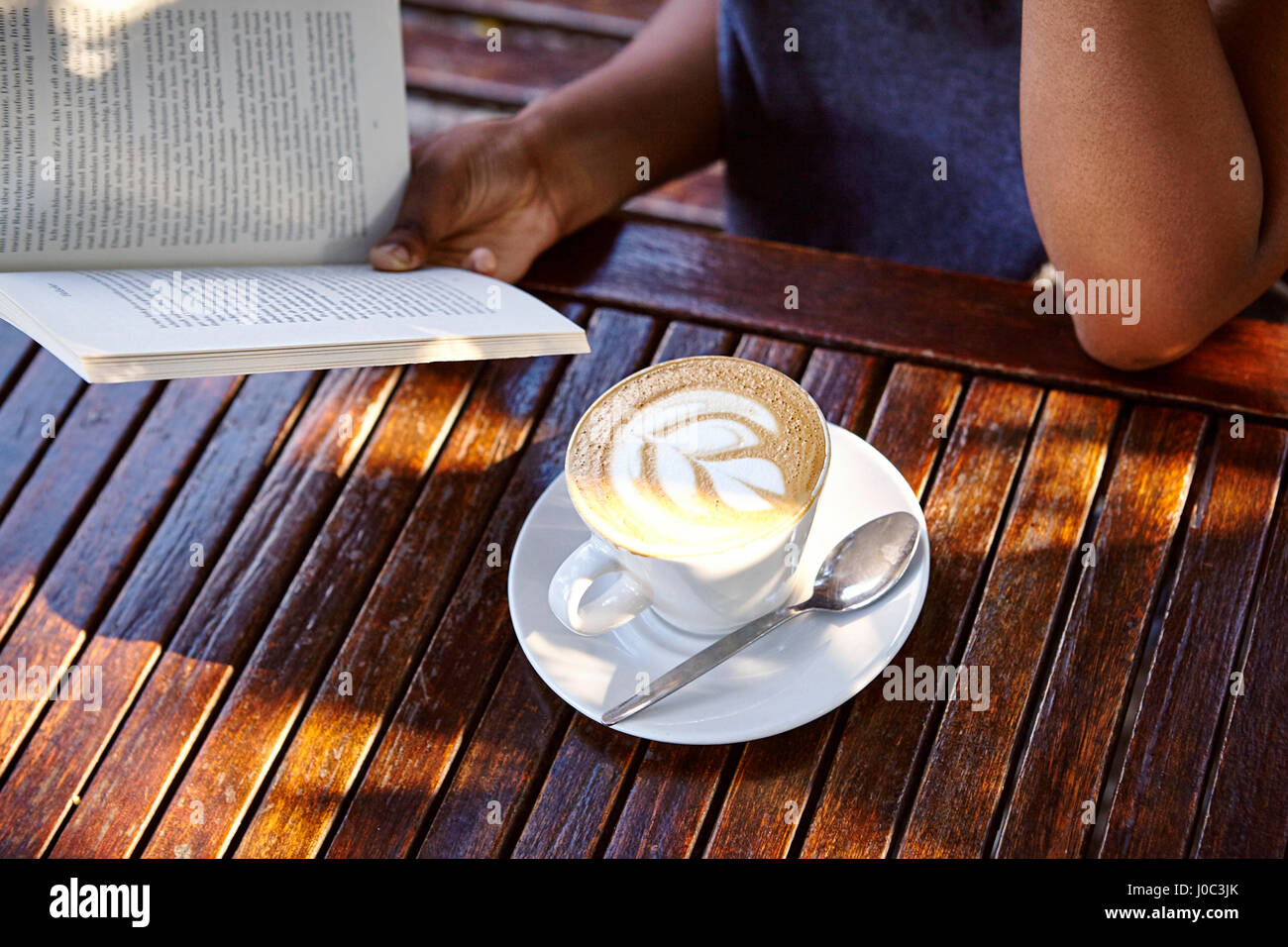 Junge Frau sitzt im Freien, Lesebuch, Kaffee vor ihr, Mittelteil Stockfoto