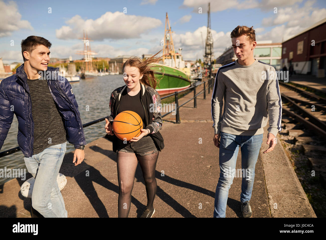 Drei Freunde, die zu Fuß neben Fluss, junge Frau, die Basketball, Bristol, UK Stockfoto