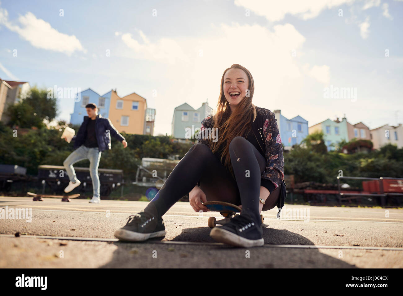 Zwei Freunde herumalbern im Freien, junge Frau sitzt auf Skateboard, lachen, Bristol, UK Stockfoto