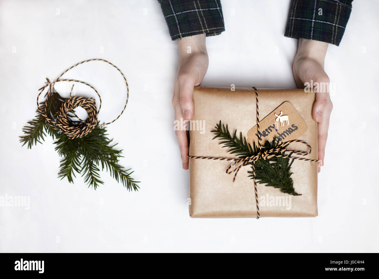 Frau mit Weihnachtsgeschenk verpackt in braunem Papier, dekoriert mit Farn und String, Draufsicht Stockfoto