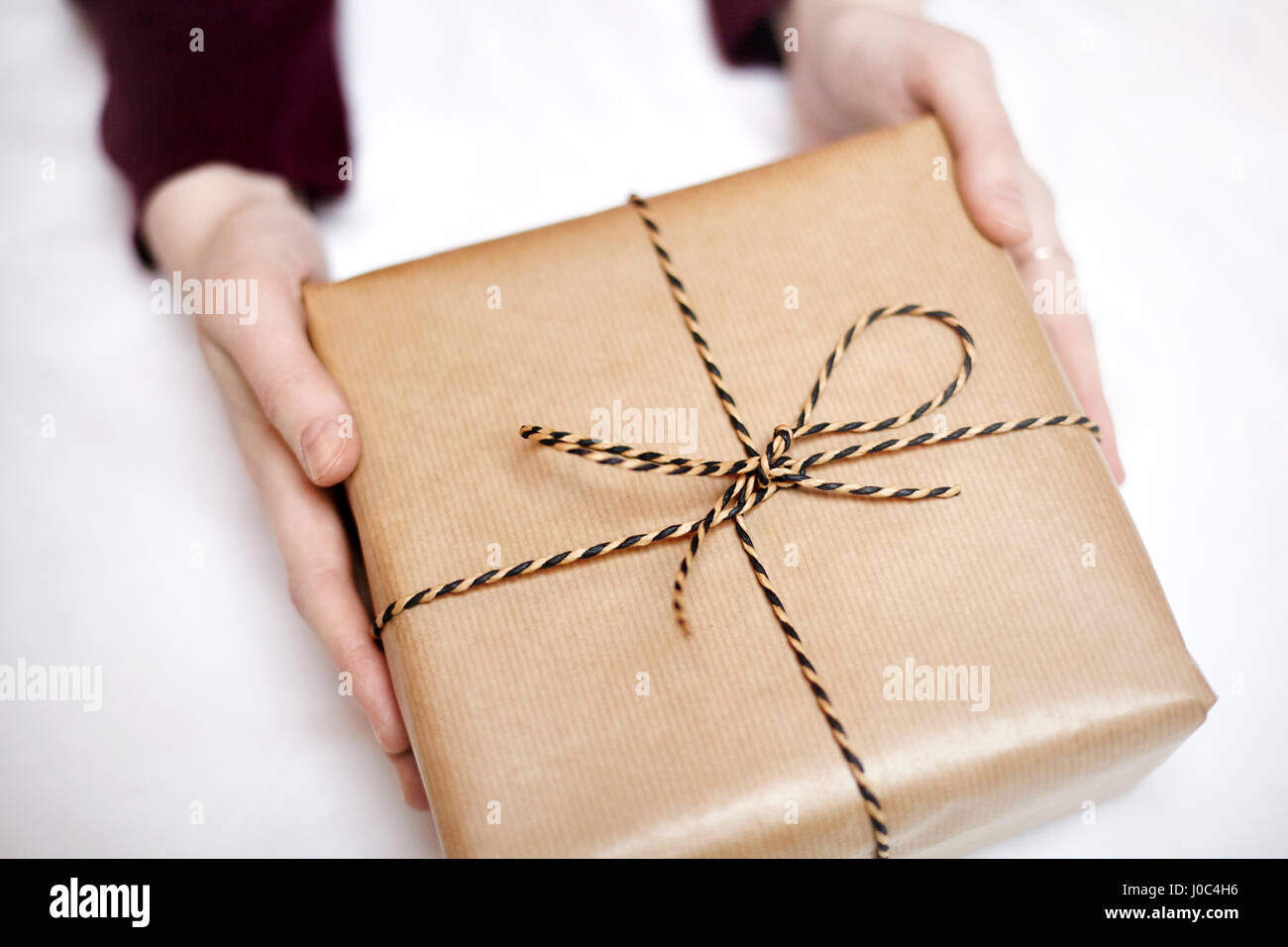 Frau mit Geschenk verpackt in Packpapier, dekoriert mit einer Schnur, Nahaufnahme Stockfoto