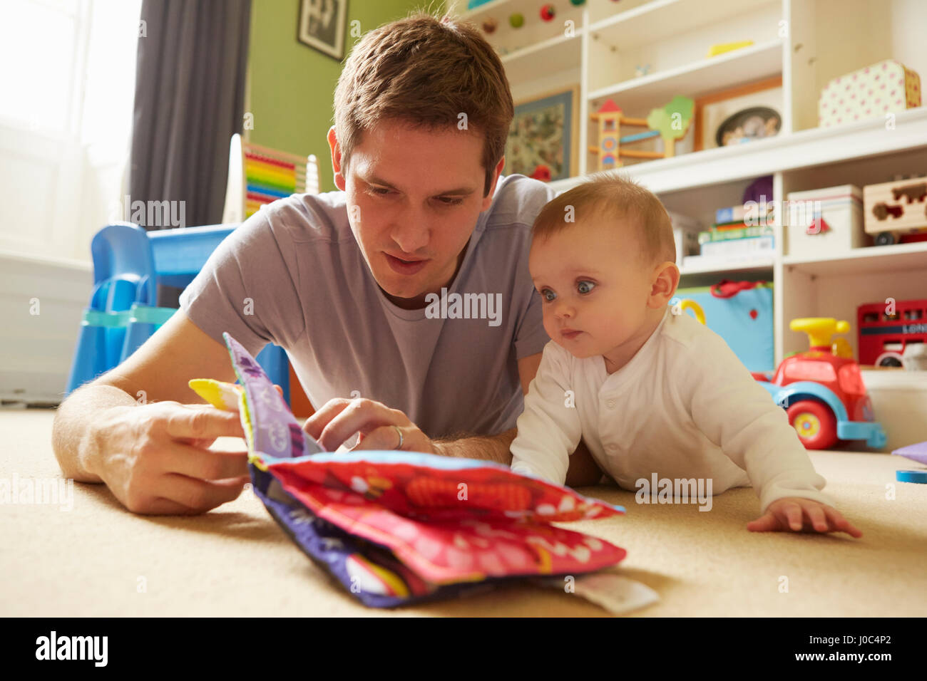 Mitte erwachsener Mann und Baby Tochter Lesung Märchenbuch im Spielzimmer Stockfoto