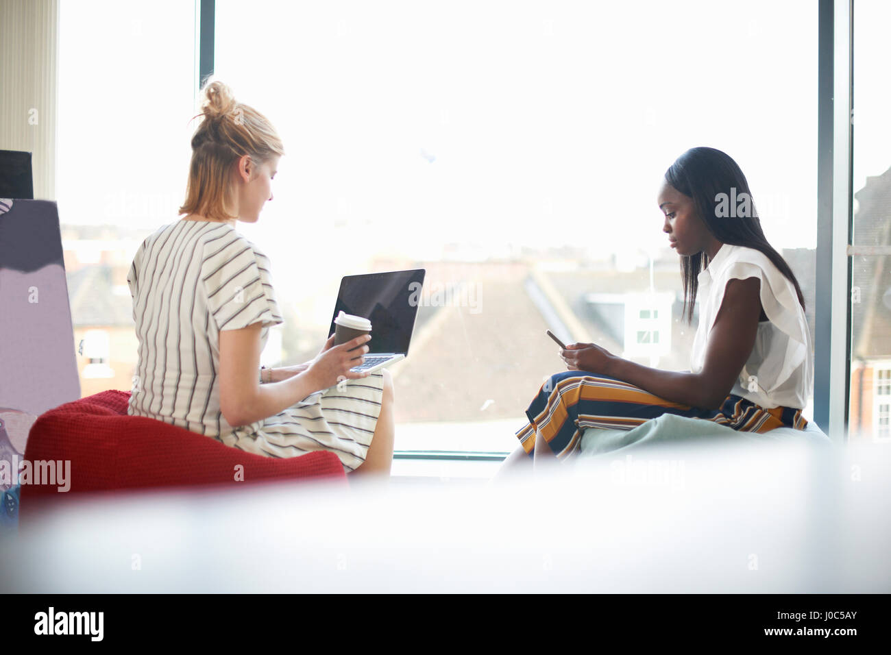 Zwei Geschäftsfrauen sitzen auf Sitzsäcke Blick auf Laptop und smartphone Stockfoto