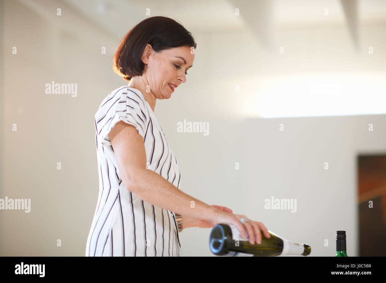 Reife Frau Gießen Weißwein bei Kunst Galerieeröffnung Stockfoto