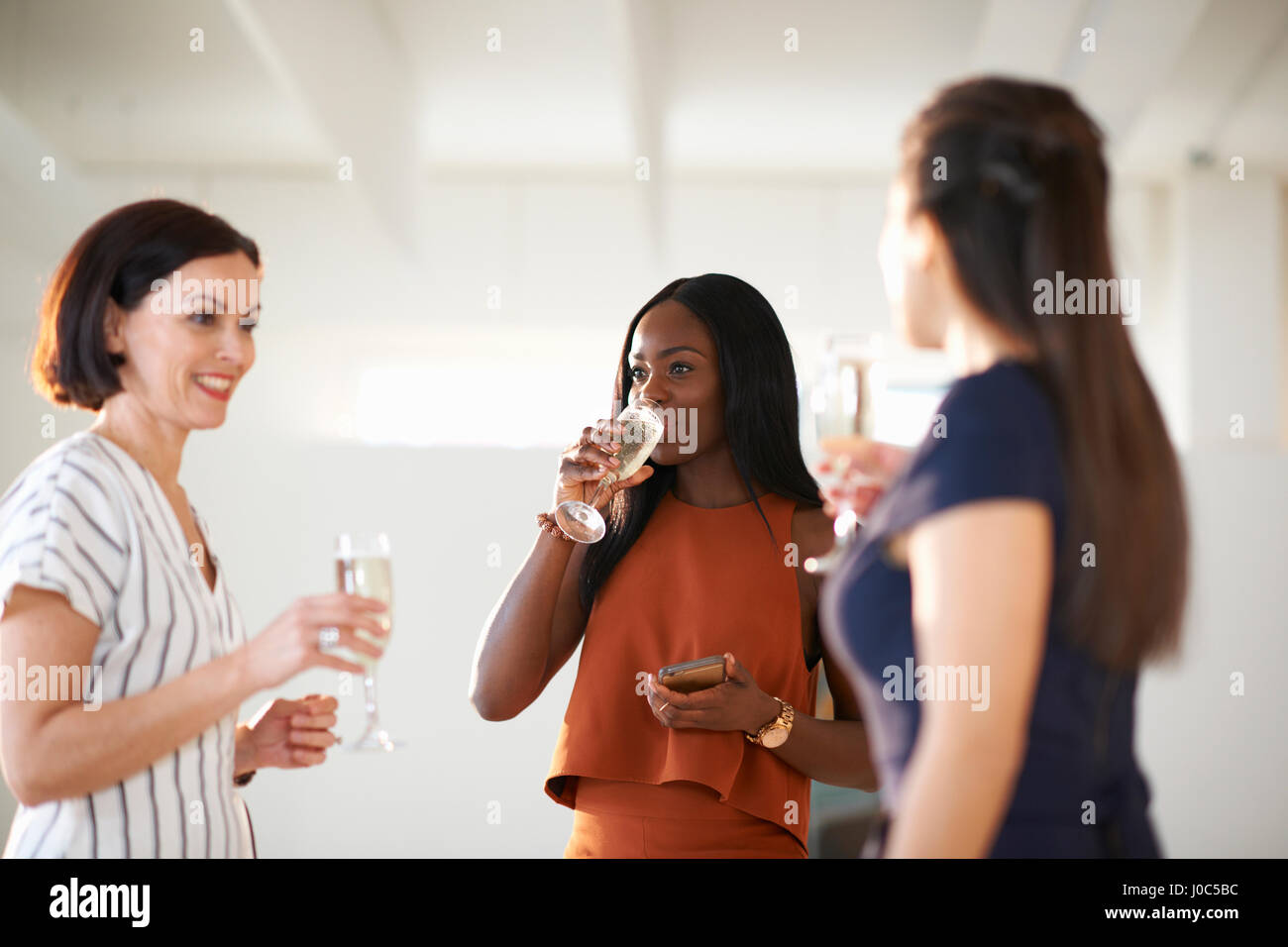 Drei Frauen plaudern und trinken Weißwein bei Kunst Galerieeröffnung Stockfoto