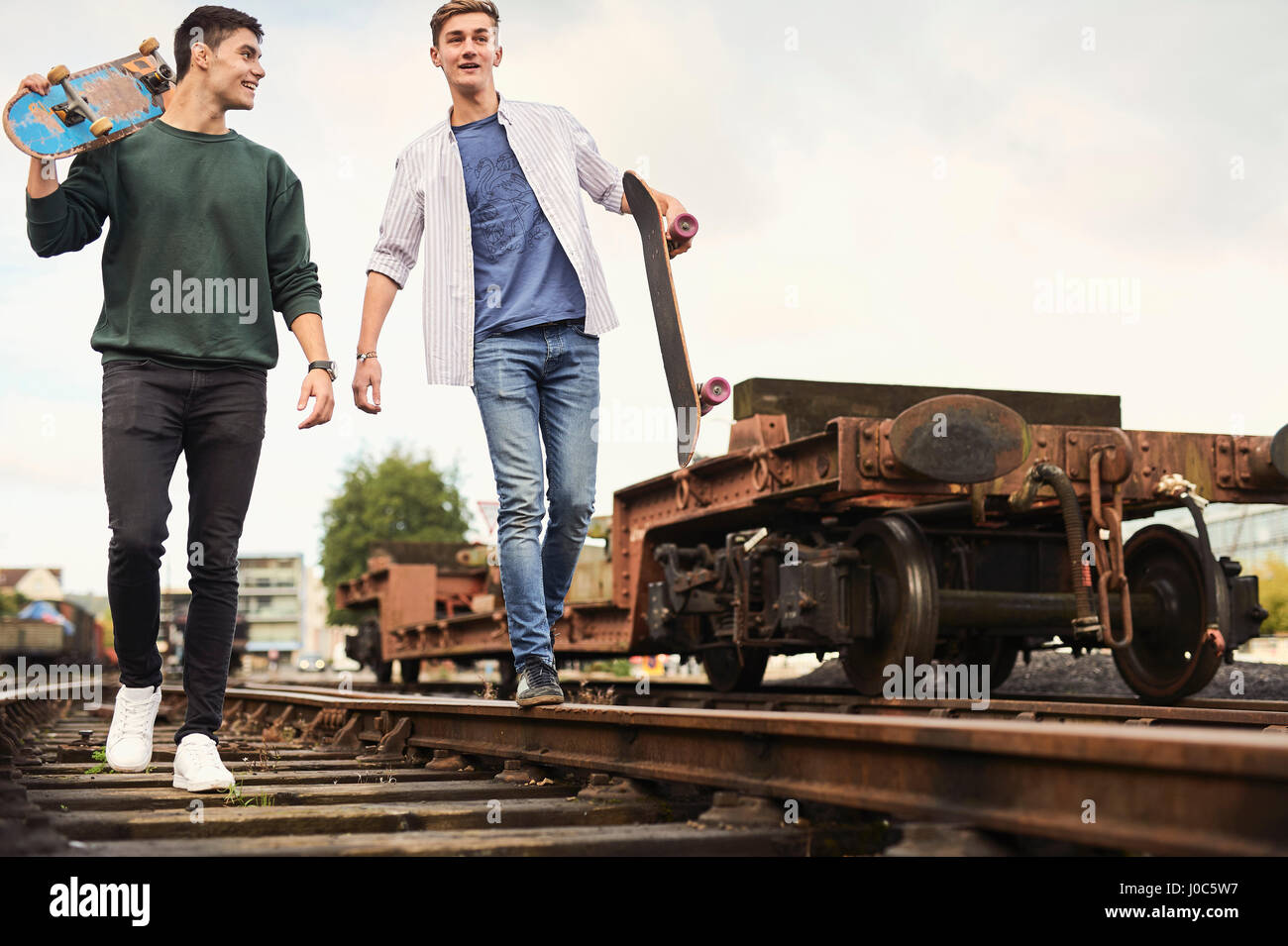Zwei junge Männer zu Fuß entlang der Bahnstrecke, mit Skateboards, Bristol, UK Stockfoto
