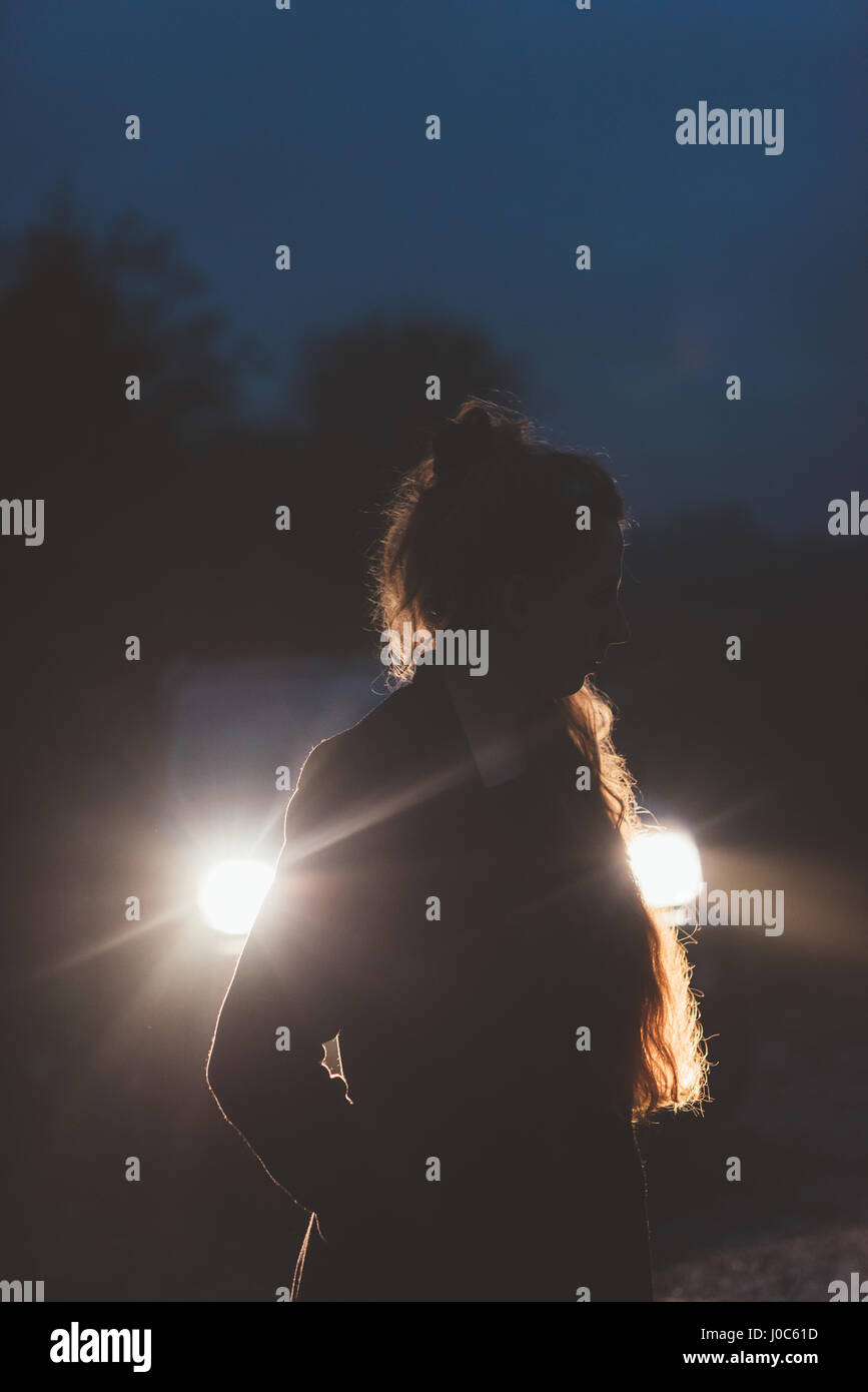 Frau vor Autoscheinwerfern am Straßenrand in der Nacht Stockfoto