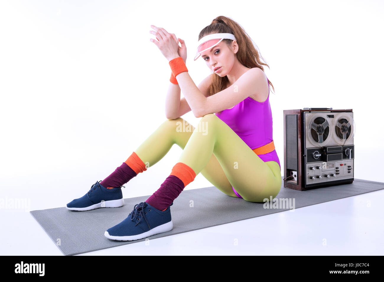 sportliche Frau sitzt auf Ausbildung Matte mit Retro-Record Player auf weiß Stockfoto