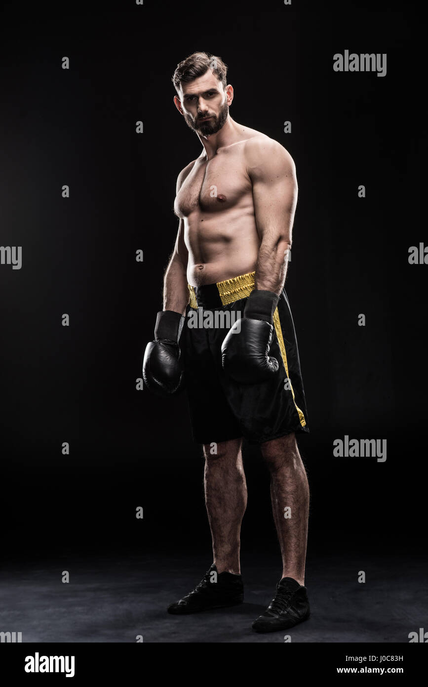 In voller Länge Portrait von muskulösen Sportler in Boxhandschuhen und Shorts posiert auf schwarz Stockfoto