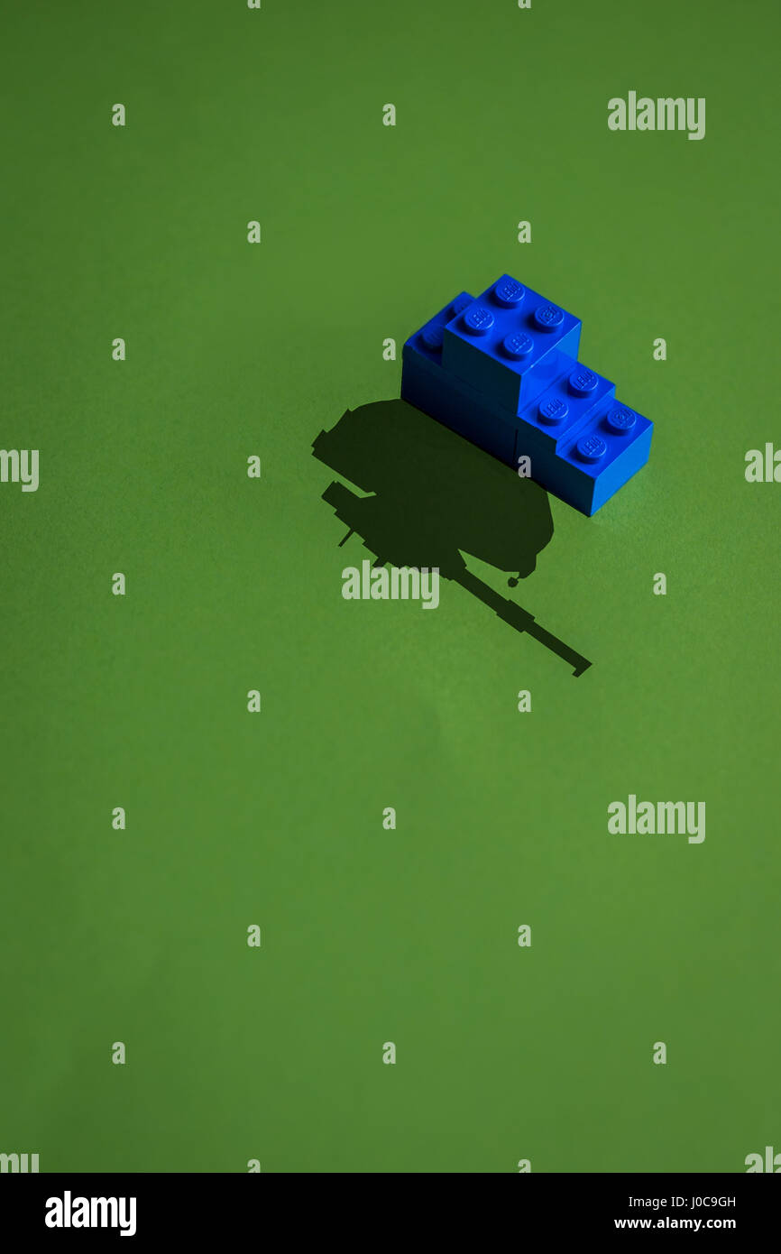 Minimalistische Tank gebaut mit blauen Lego mit einem Schatten von echten Panzer auf eine grüne Schrift Stockfoto
