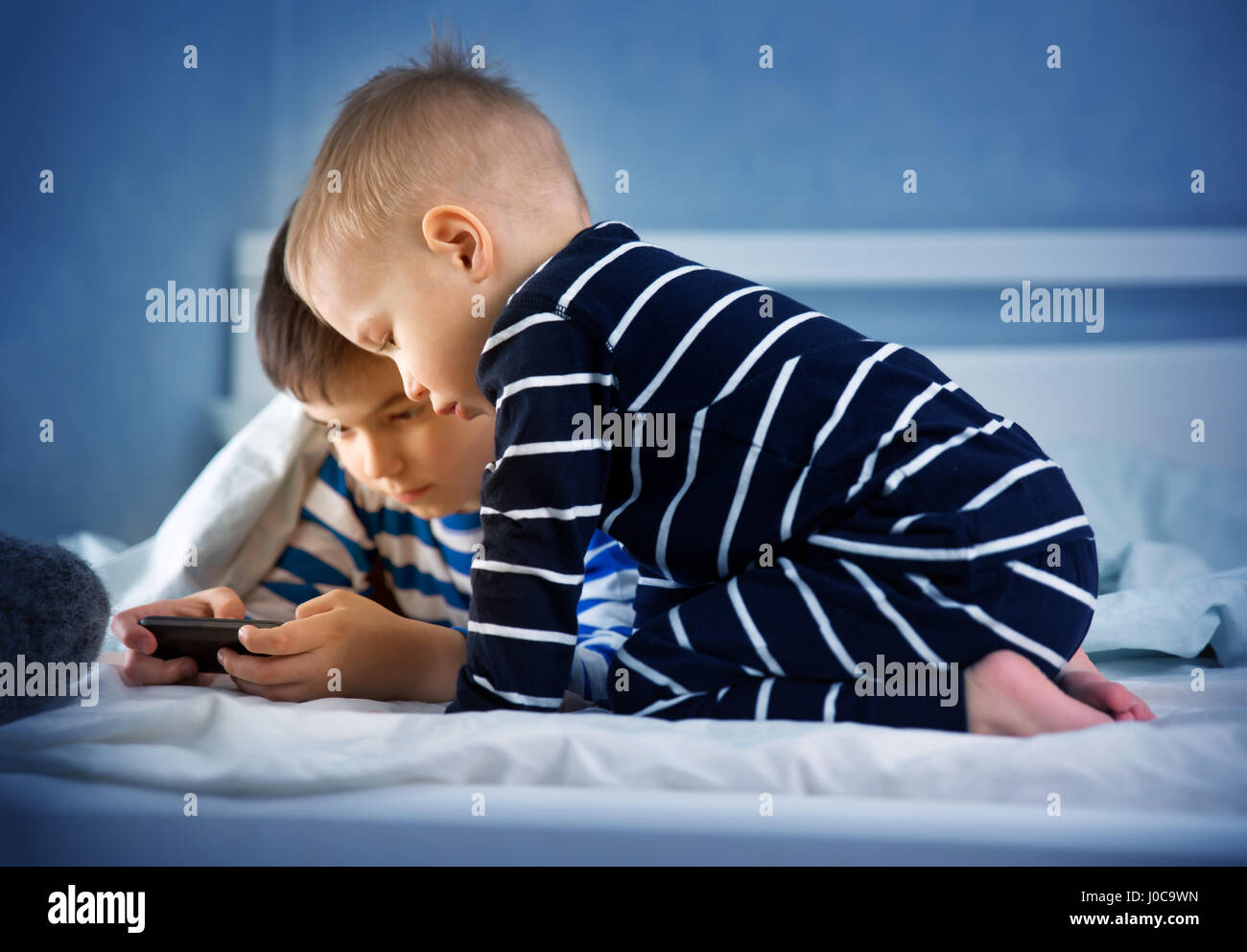 Jungs im Bett liegen und spielen im Smartphone. Kinder beobachten Film in der Nacht Stockfoto