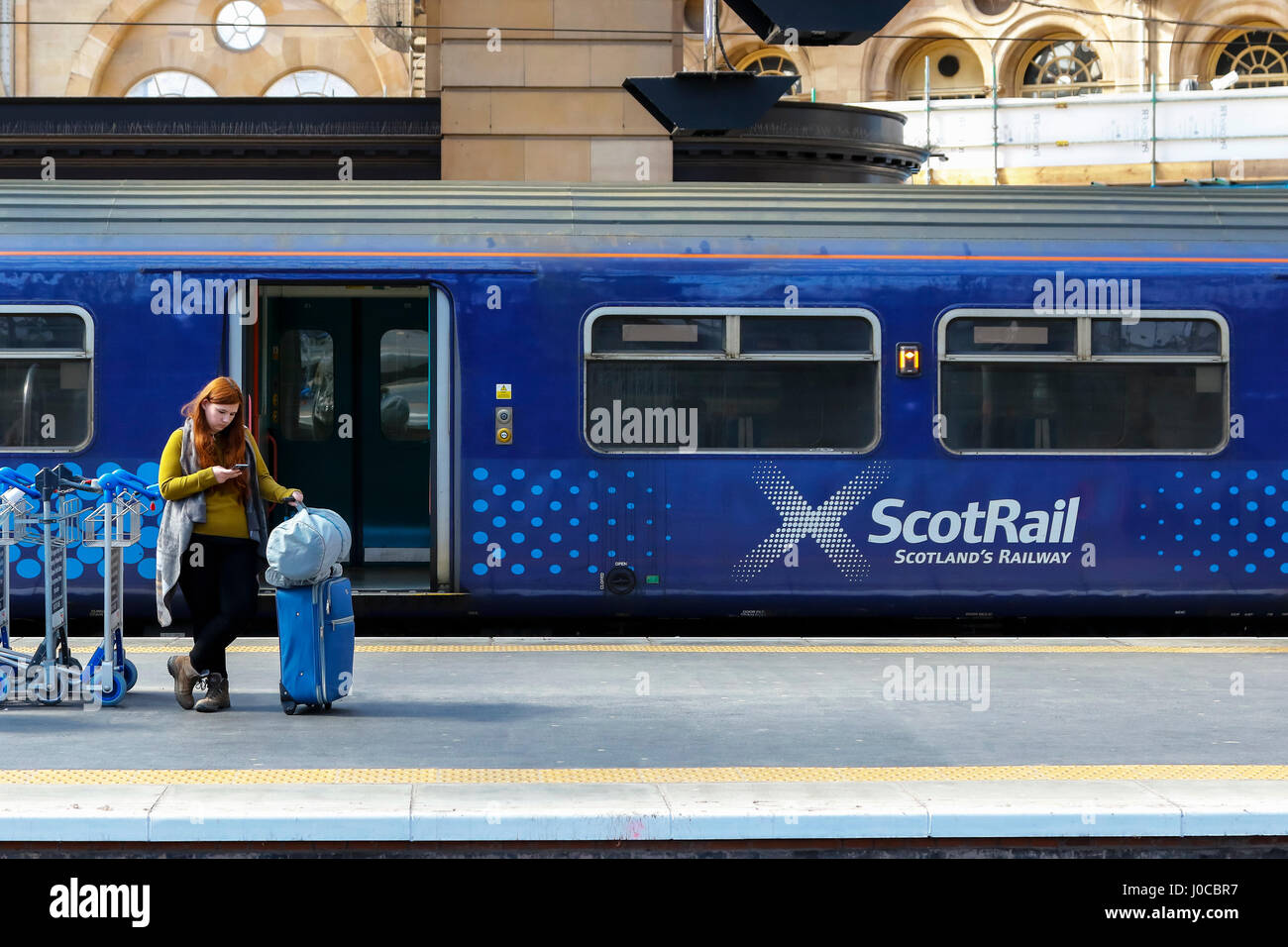 Frau wartet auf der Plattform am Hauptbahnhof von Glasgow, Glasgow mit einem scotrail Schlitten hinter ihr. Glasgow, Schottland, Großbritannien Stockfoto