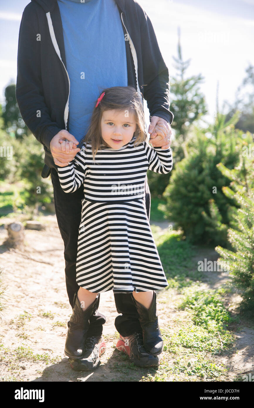 Porträt von kleinen Mädchen Hand in Hand des Vaters und von Tannen auf seinen Füßen stehen Stockfoto