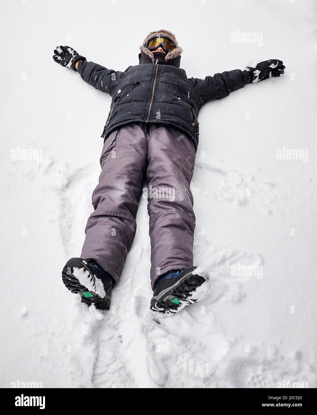 Junge auf Rücken auf schneebedeckten Boden liegend Stockfoto